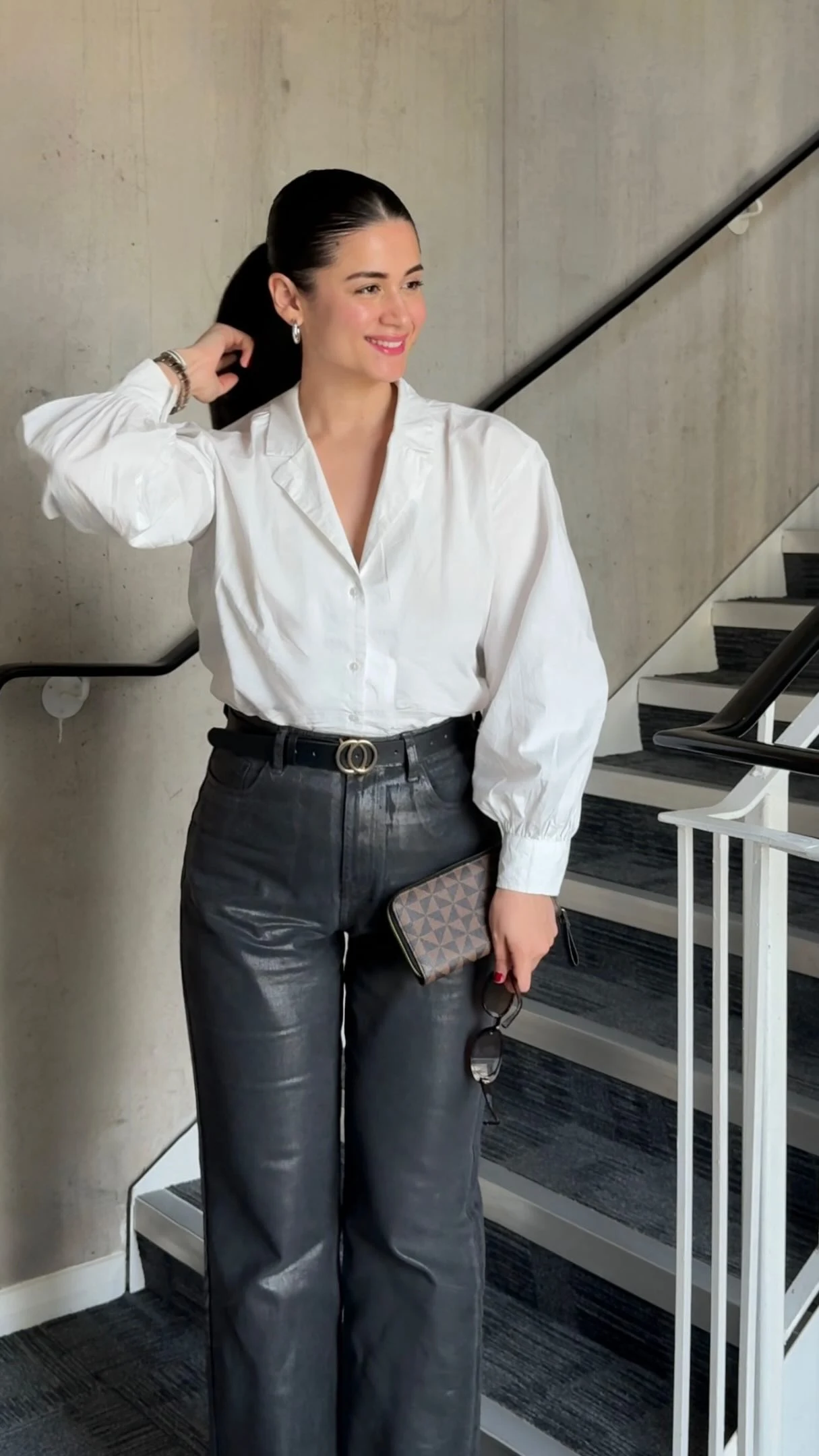 Tucked white button-up shirt paired with high-waisted black leather trousers, gold belt, and silver heels.