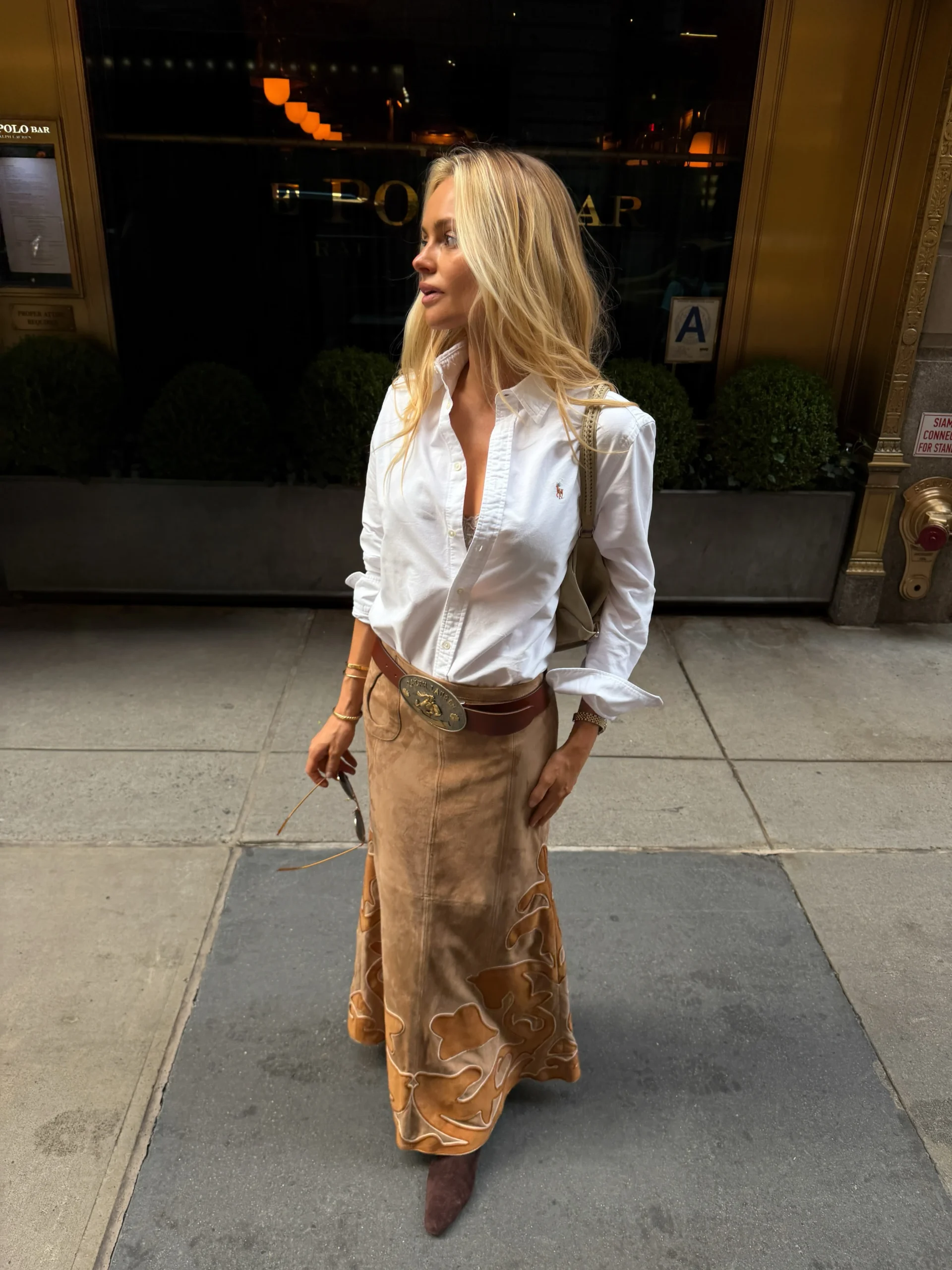Woman wearing a white button-down, tan suede maxi skirt with horse applique, leather belt, and brown ankle boots.