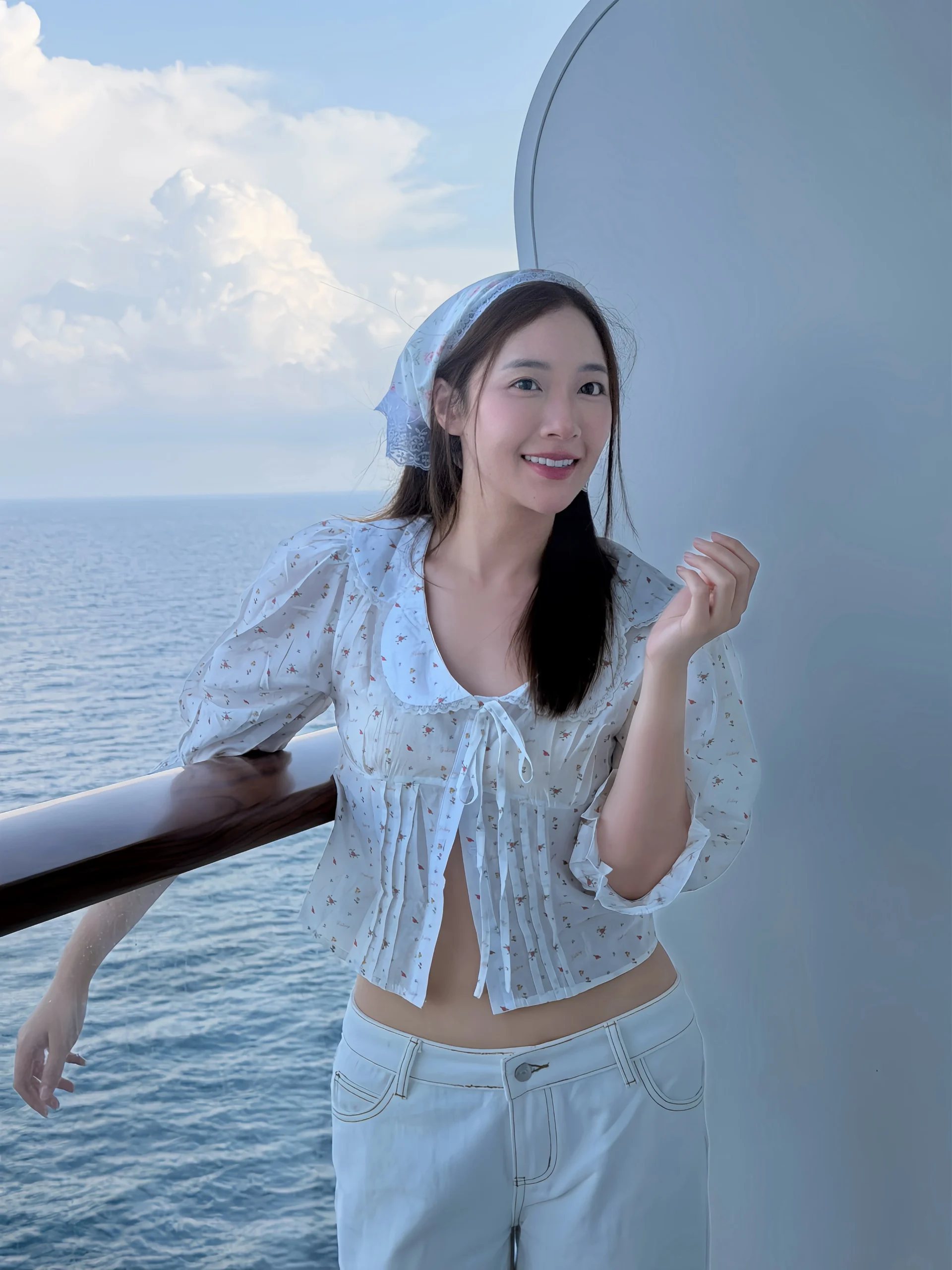 Woman wearing a white cropped floral blouse, wide-leg pants, and a light headscarf.