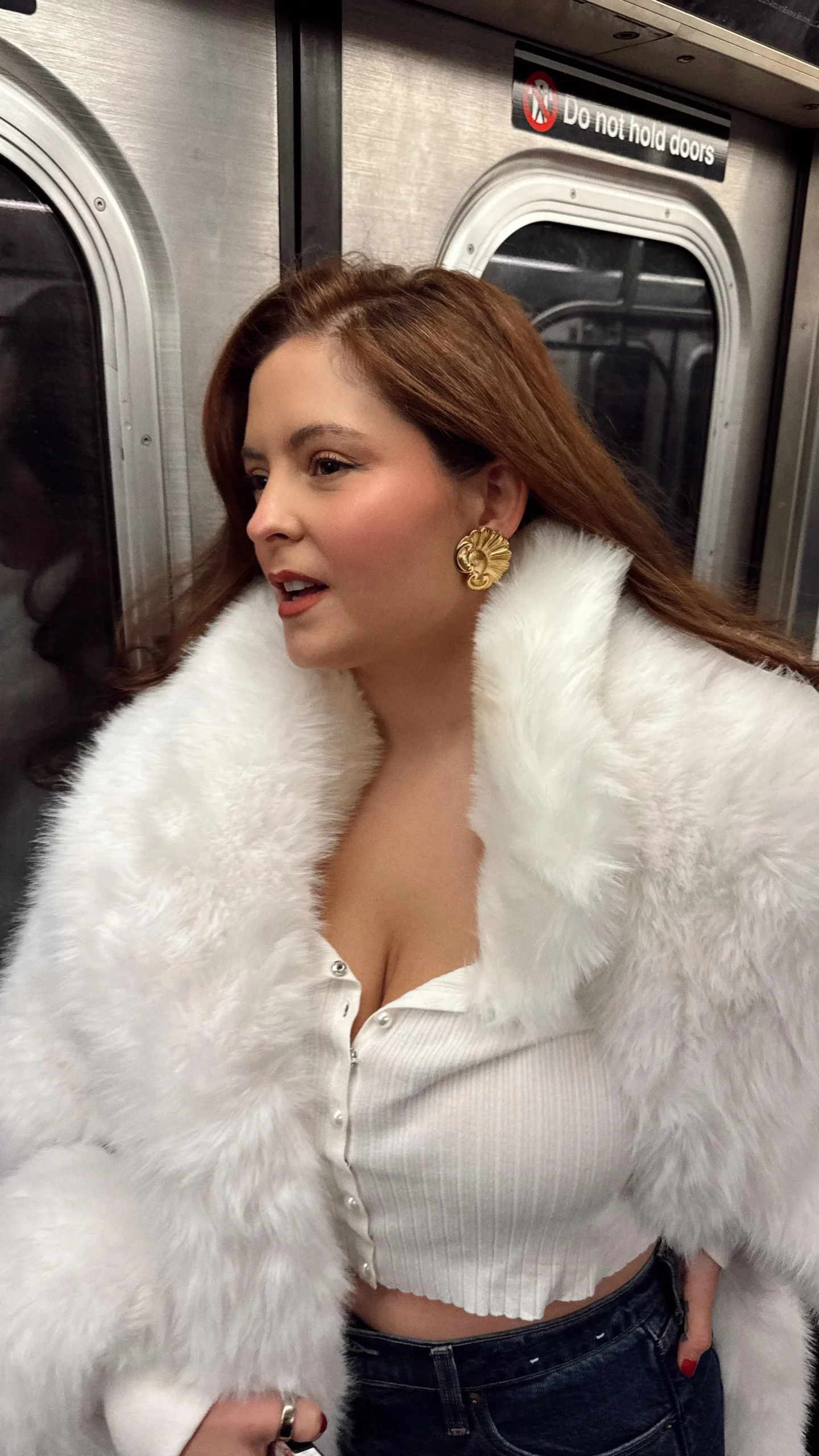 Person in a white fluffy-collar coat over a ribbed crop top and dark blue jeans with a gold earring.