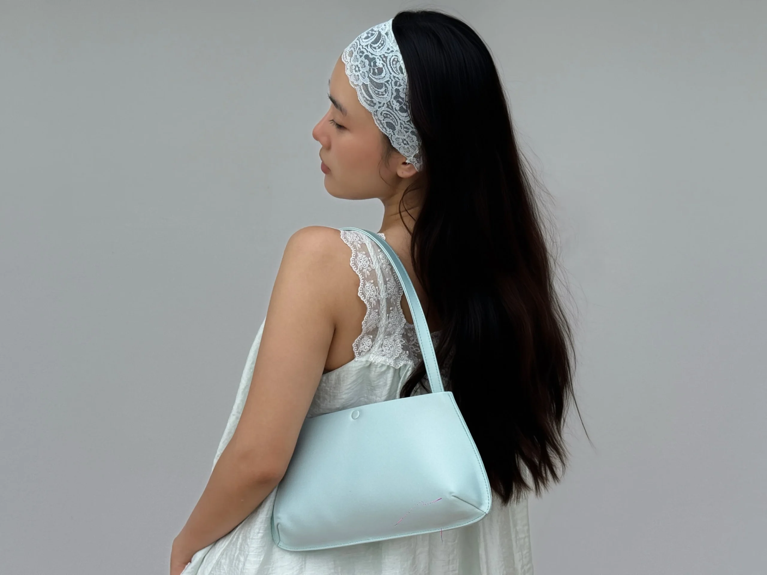 Flowing white sleeveless dress with lace straps, a white lace headband, and a pale blue shoulder bag.