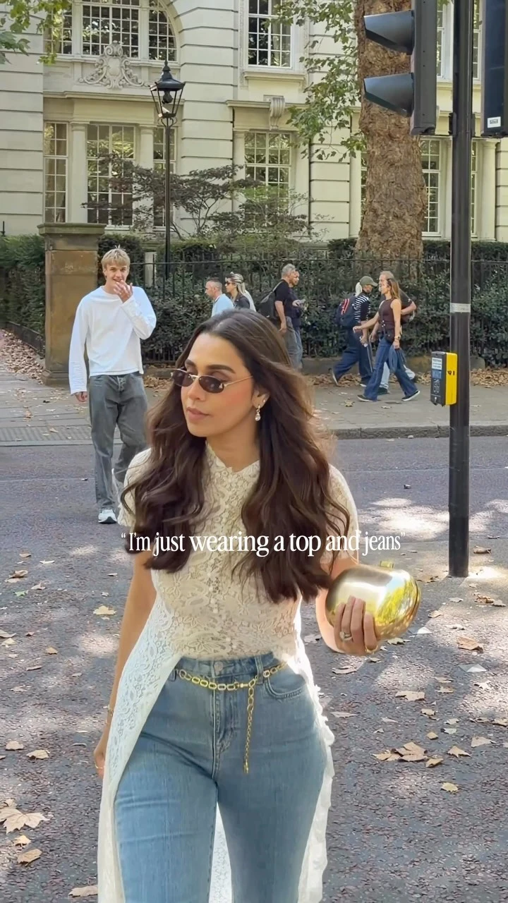 Woman in a white lace top, light-blue flared jeans, gold chain belt, and white shoes.