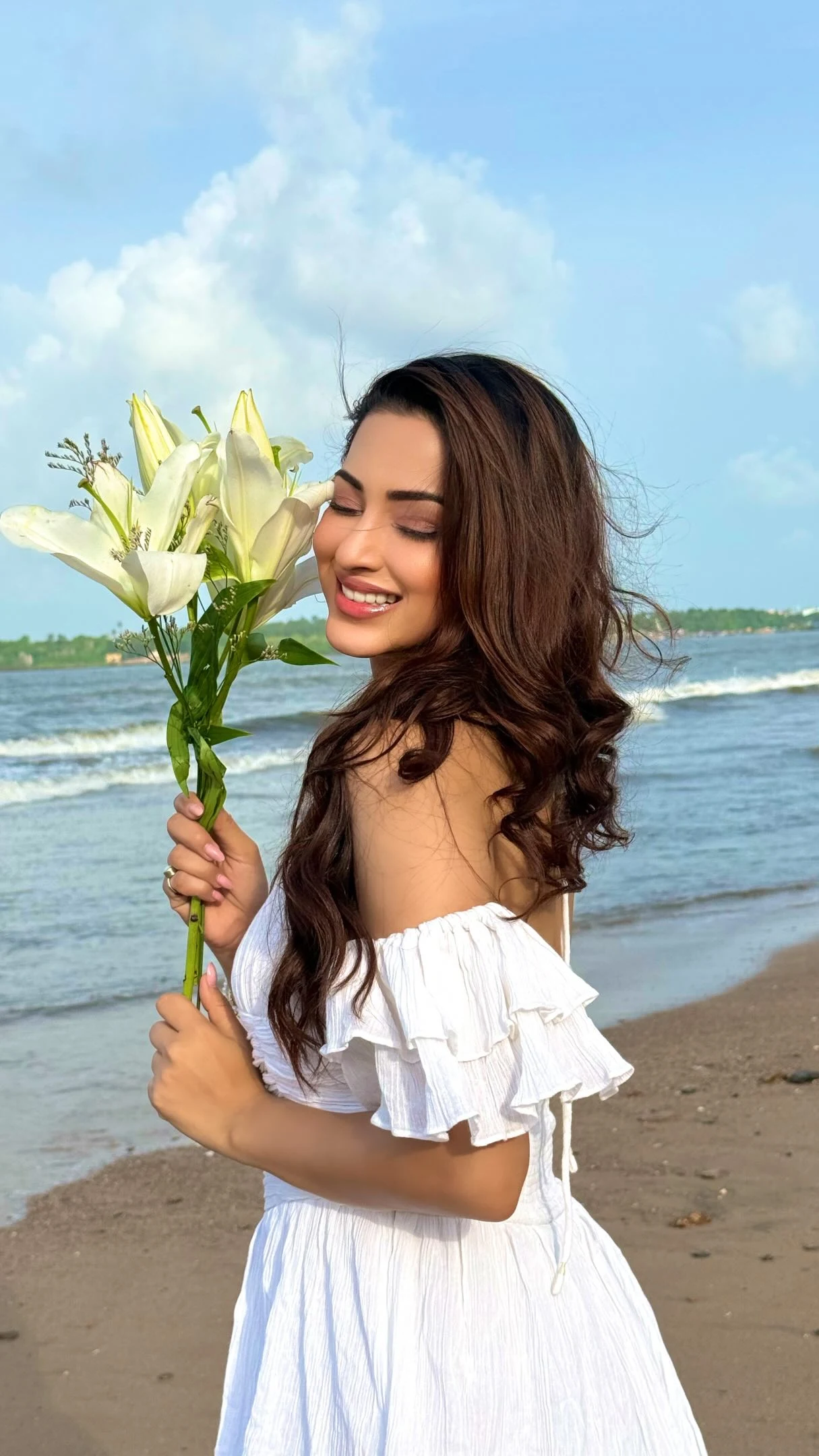 Woman wearing a white off-the-shoulder ruffled tiered maxi dress with flowing layers.