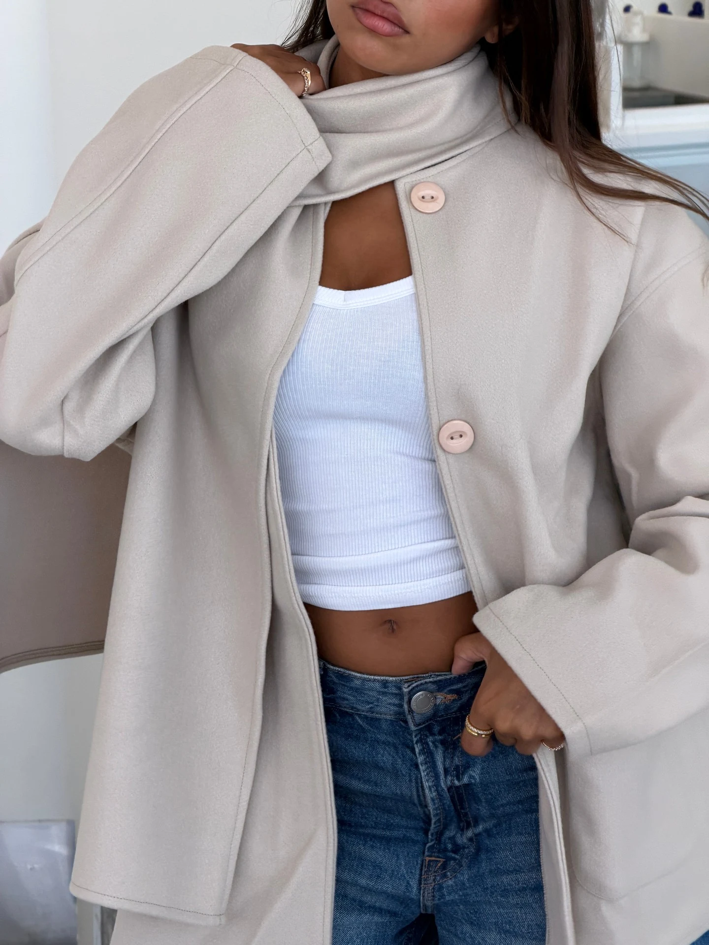 Light beige oversized wool coat with large buttons and attached detachable scarf, light blue jeans, brown handbag