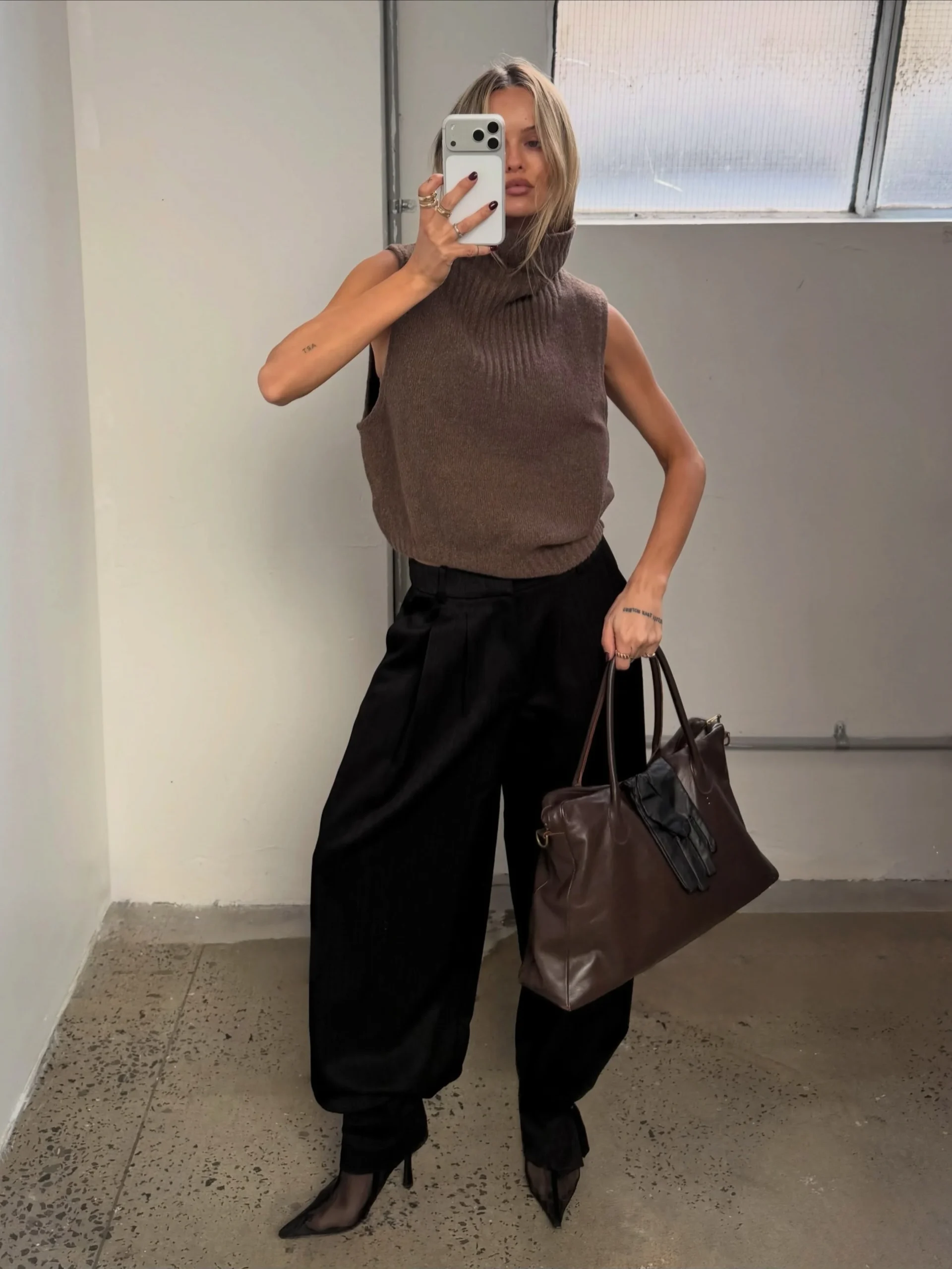 Woman wearing a black long-sleeve top, light-wash wide-leg jeans, white sneakers, and a black shoulder bag.