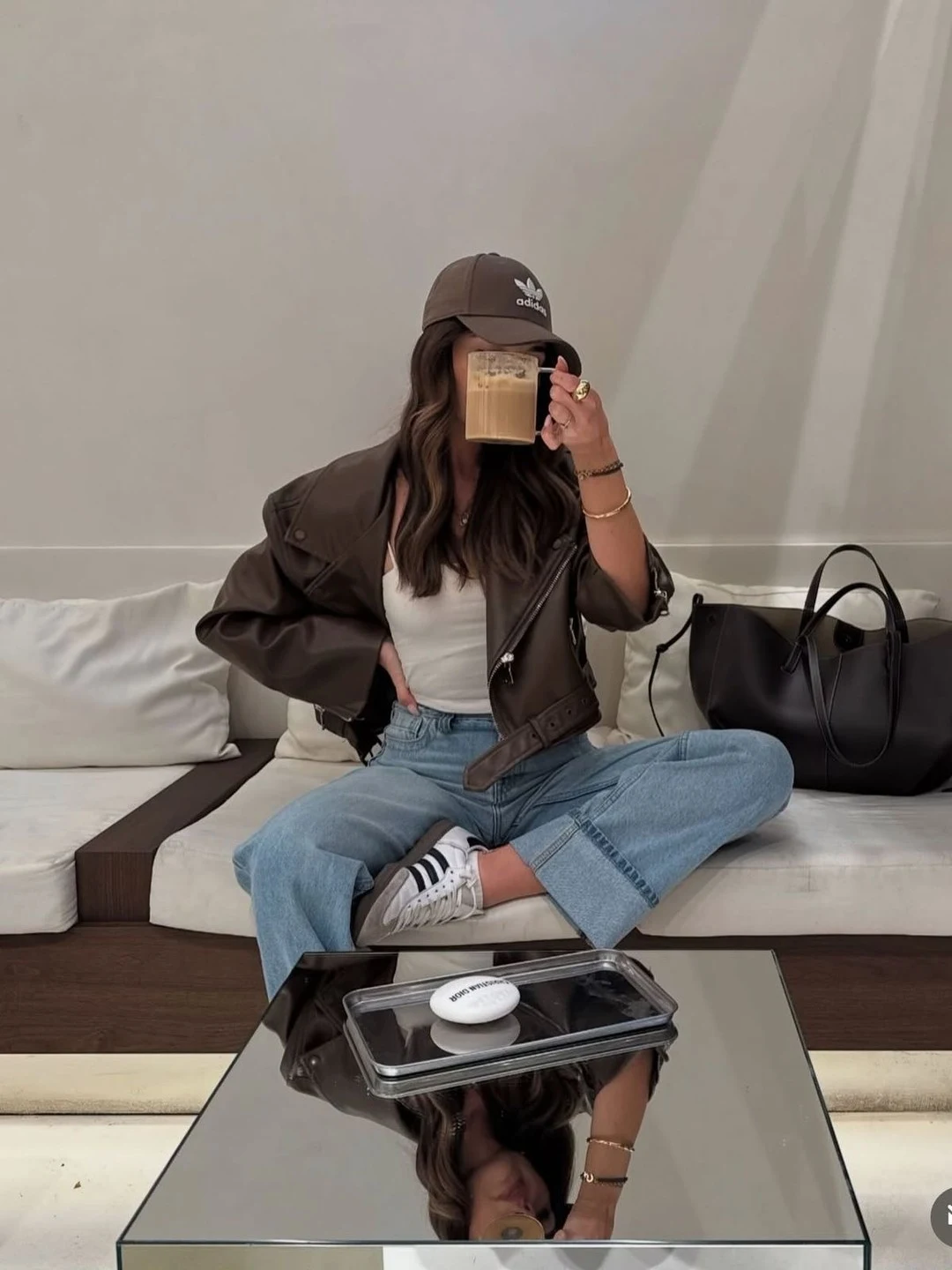 Oversized brown leather jacket and wide-leg jeans with white Sambas and a matching brown cap.
