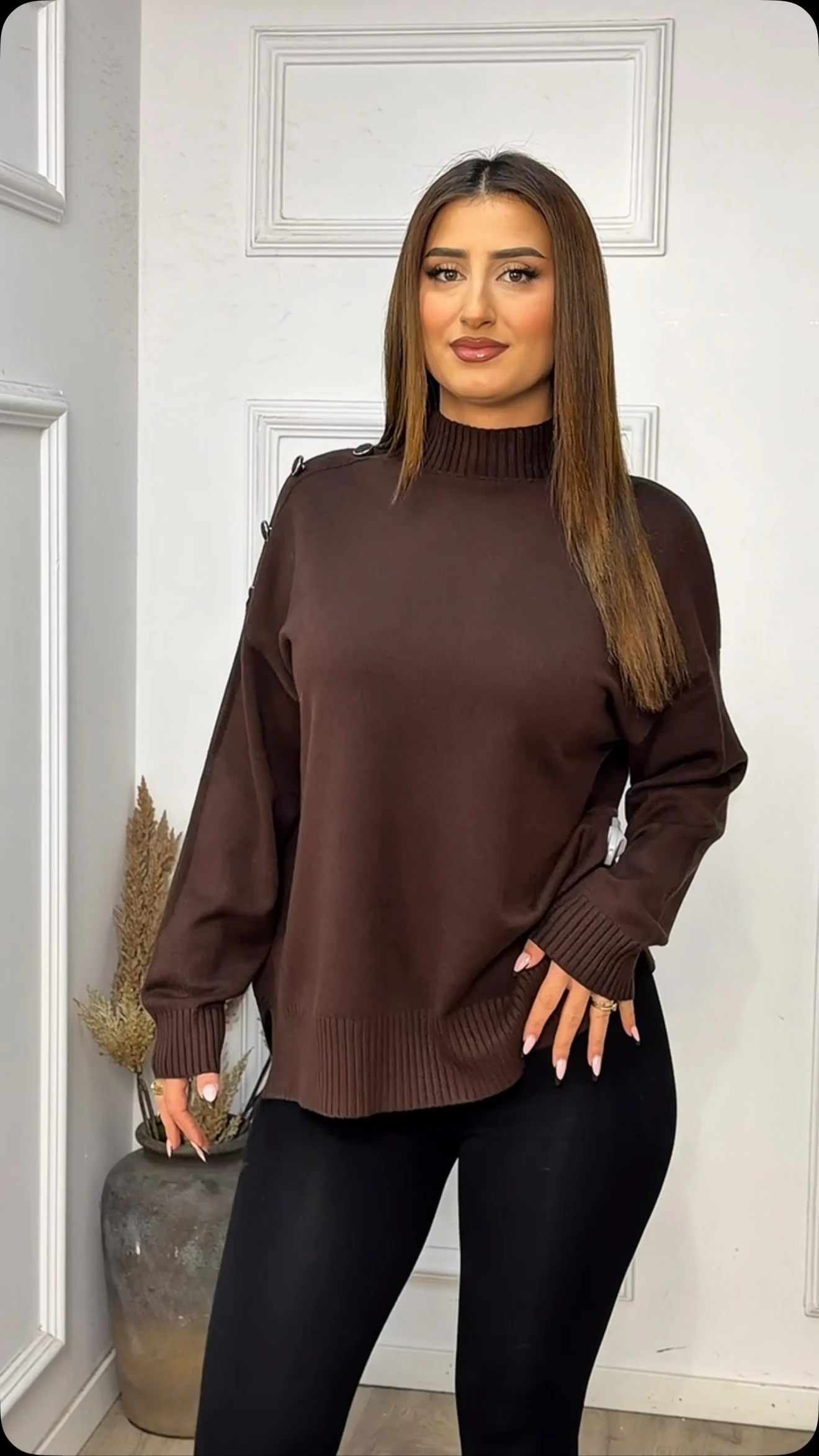 Dark brown oversized ribbed turtleneck sweater paired with fitted black leggings, model wearing several rings.