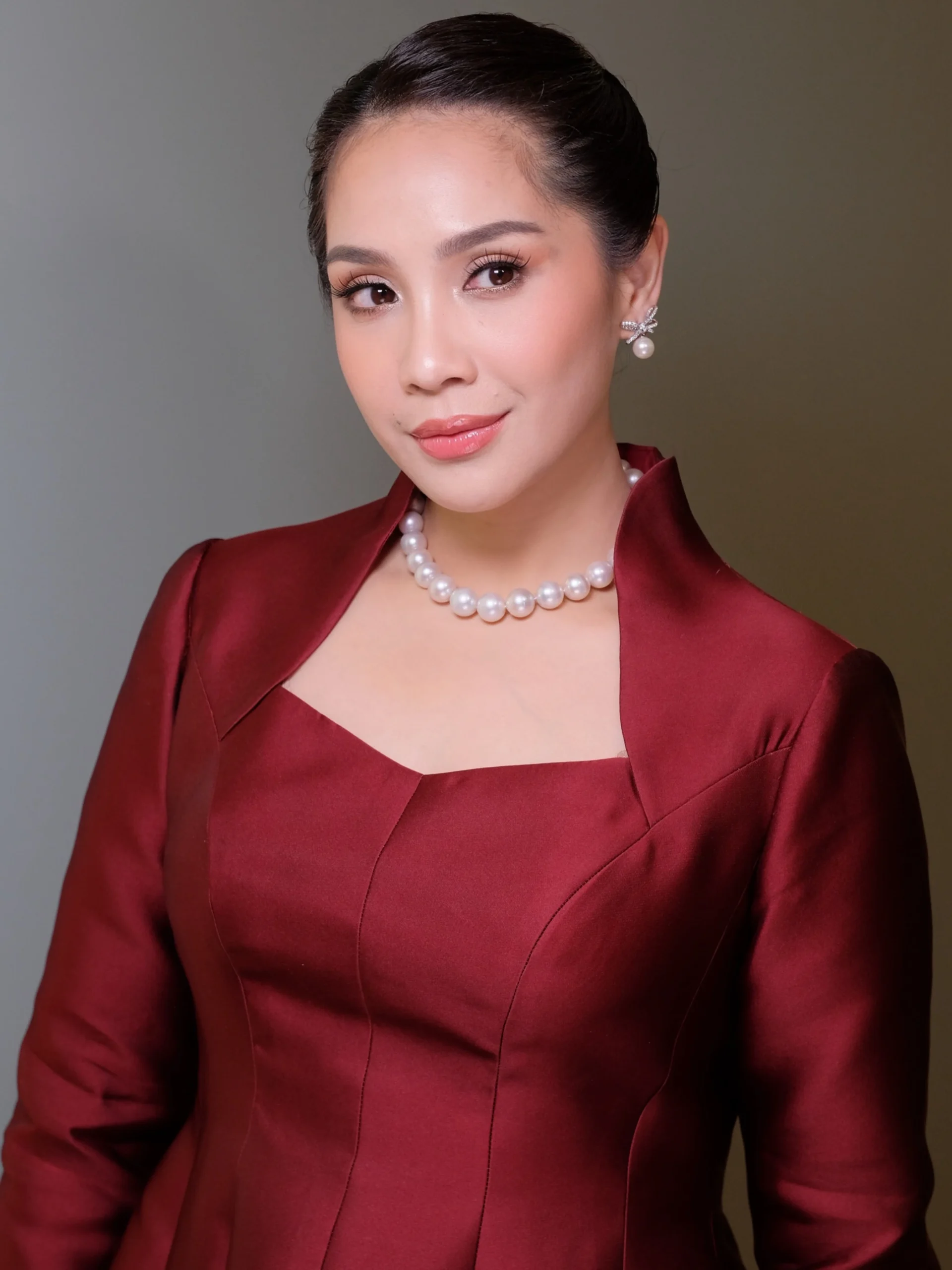 Deep burgundy fitted dress and structured jacket styled with large pale pearl necklace and earrings.