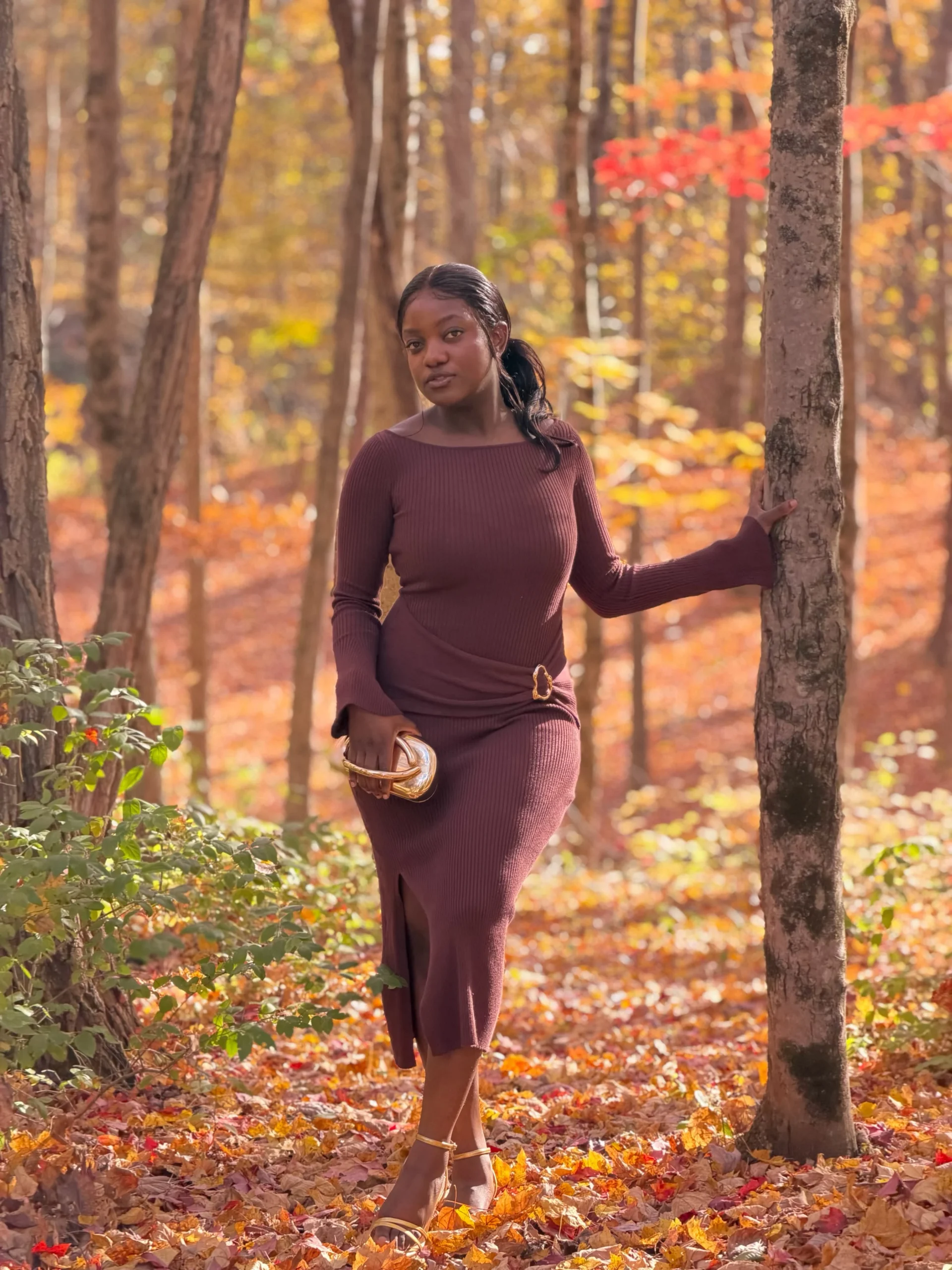 Woman in a fitted burgundy ribbed midi dress with gold strappy heels and a small gold clutch.