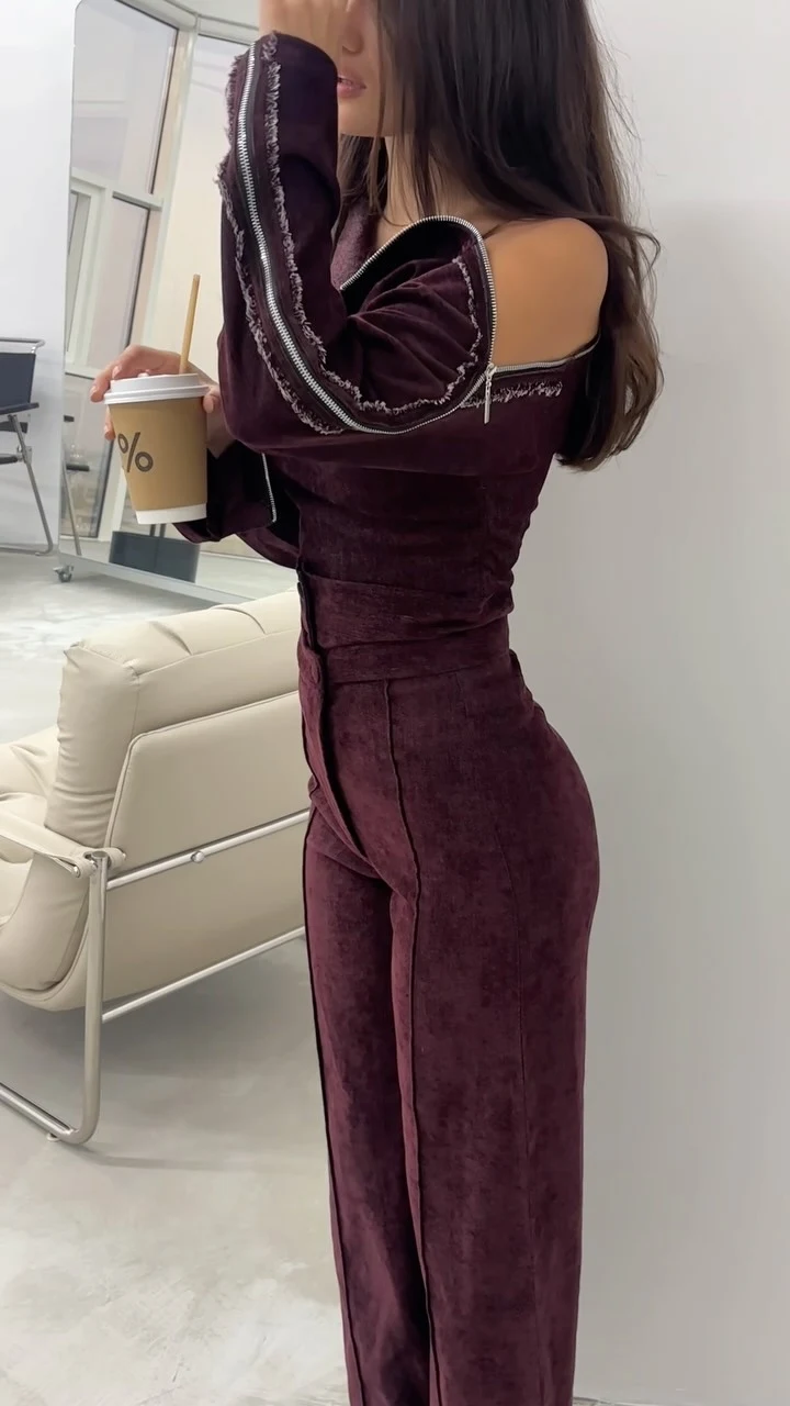 Fitted burgundy off-shoulder jumpsuit with silver zipper sleeve and neckline details.