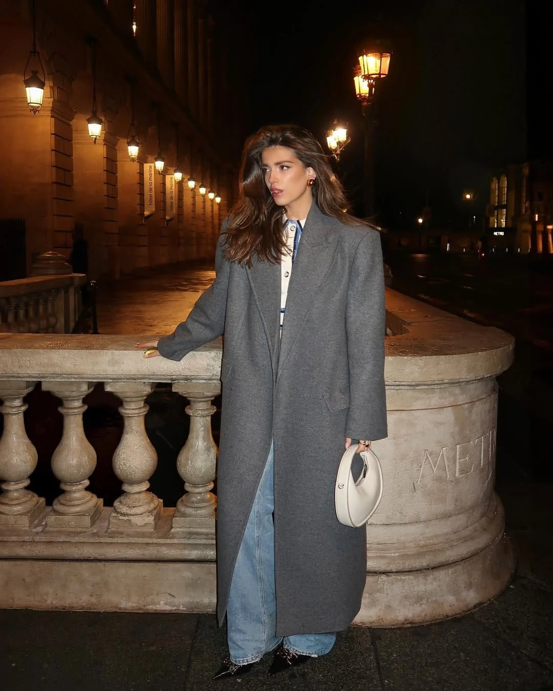 Charcoal grey long coat over a button-down shirt and jeans, finished with black booties and a white clutch.