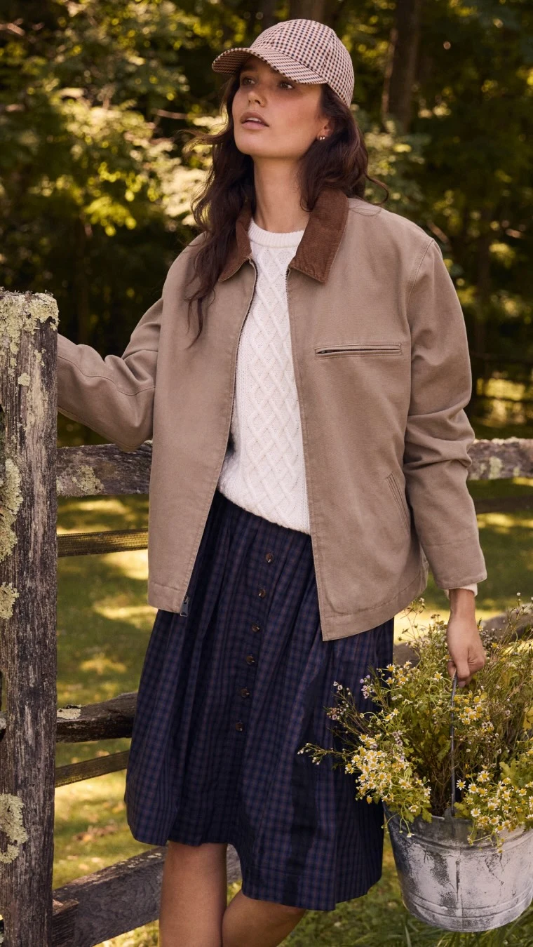 cream cable knit sweater, tan utility jacket, navy pleated midi skirt, brown and white houndstooth baseball cap, galvanized metal bucket with dried flowers