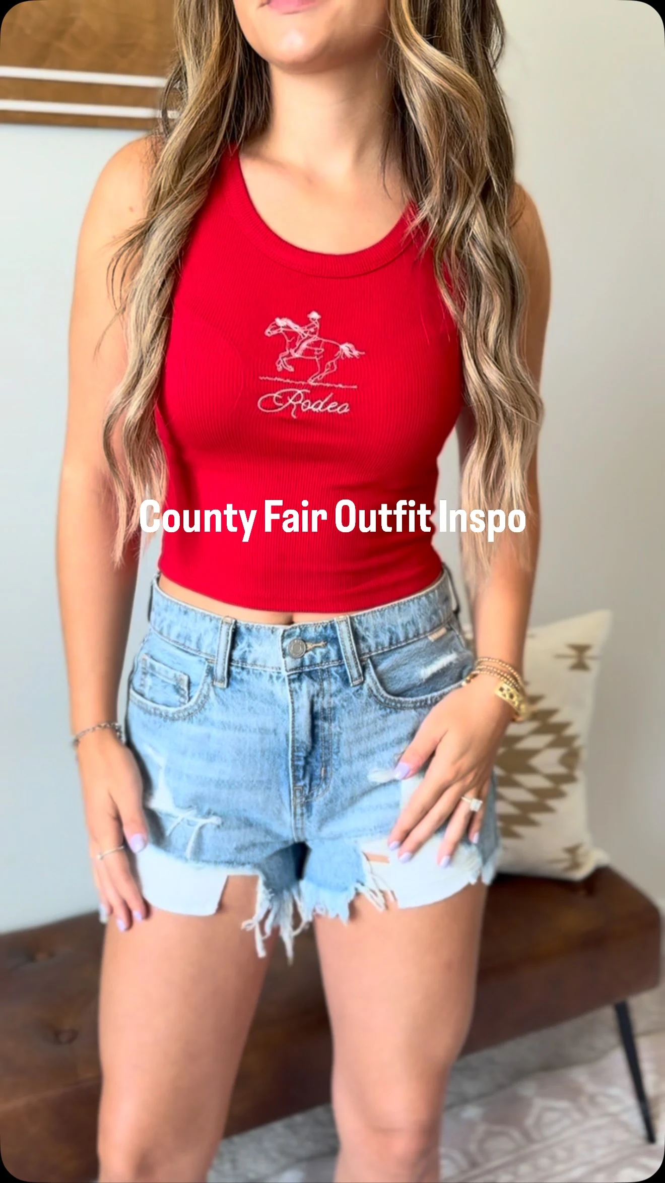 Woman wearing a cropped red ribbed Rodeo graphic tank top and light-wash distressed denim shorts.