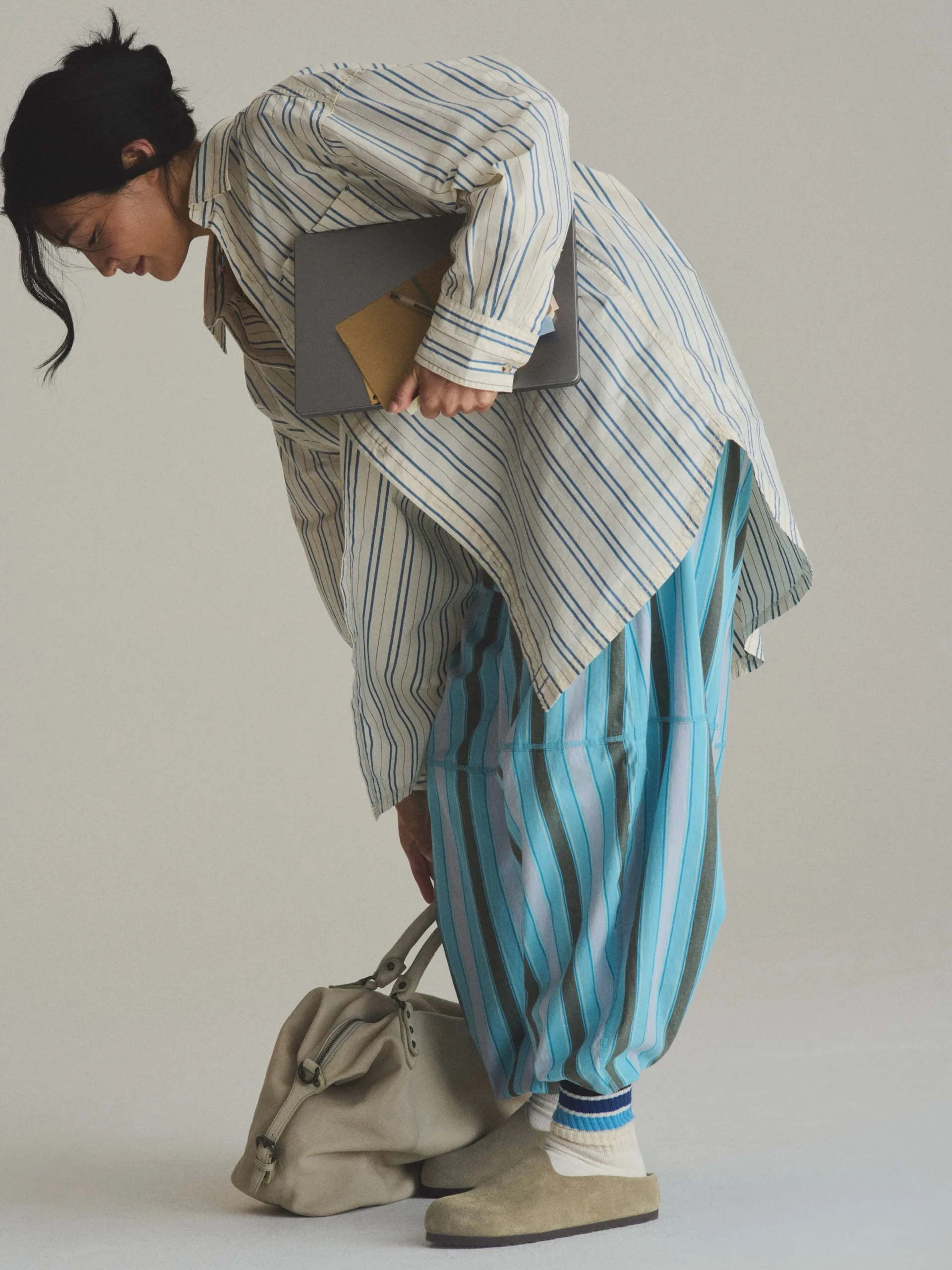 Person in a white lace midi dress and beige bomber jacket wearing ribbed socks and black Amsterdam clogs.