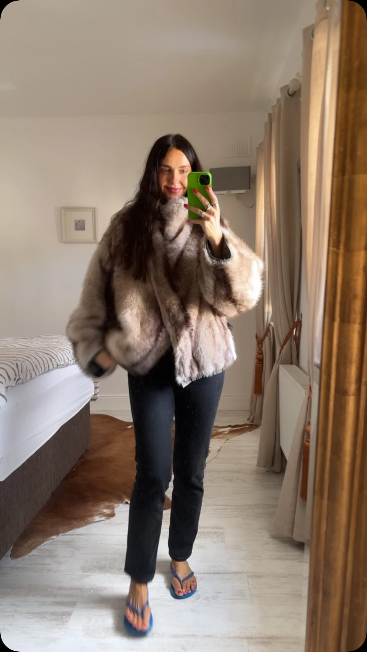Woman wearing an oversized brown and gray faux-fur coat, black skinny jeans, and blue flip-flops.