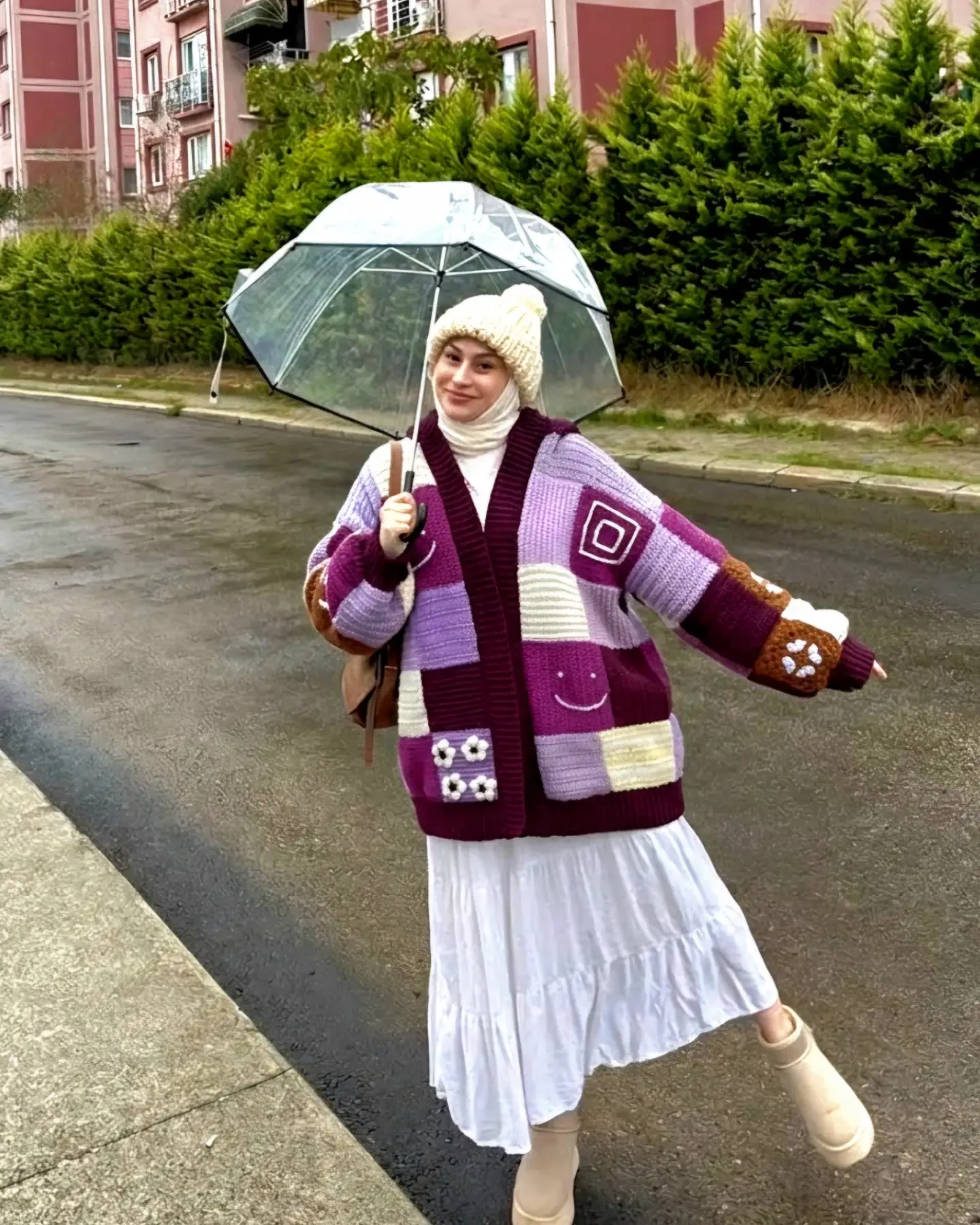 Oversized patchwork plum cardigan layered over a white tiered dress with beige boots and a cream hat.