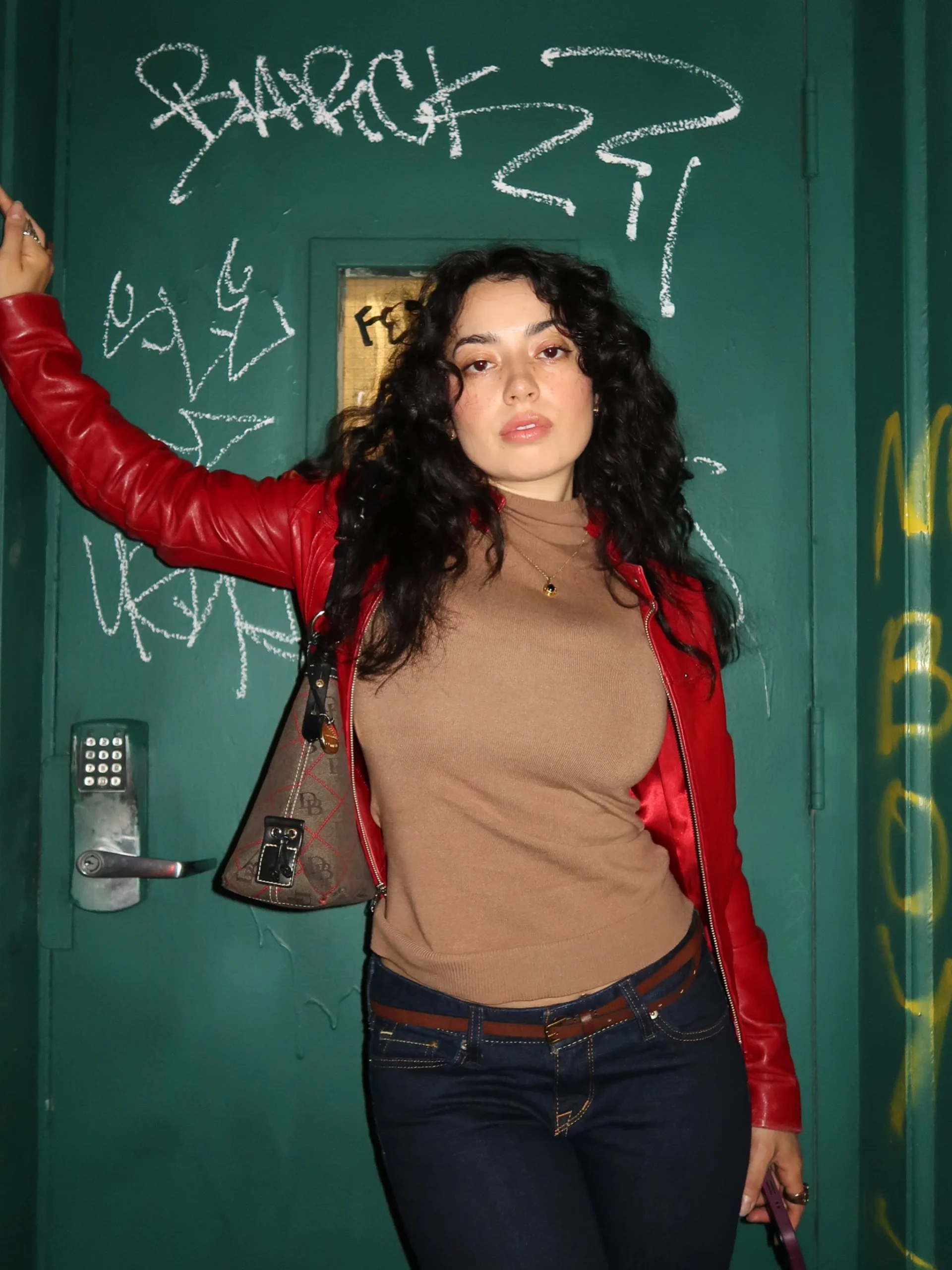 bright red leather moto jacket open over brown turtleneck, dark blue jeans, brown monogram crossbody bag, black square-toe boots