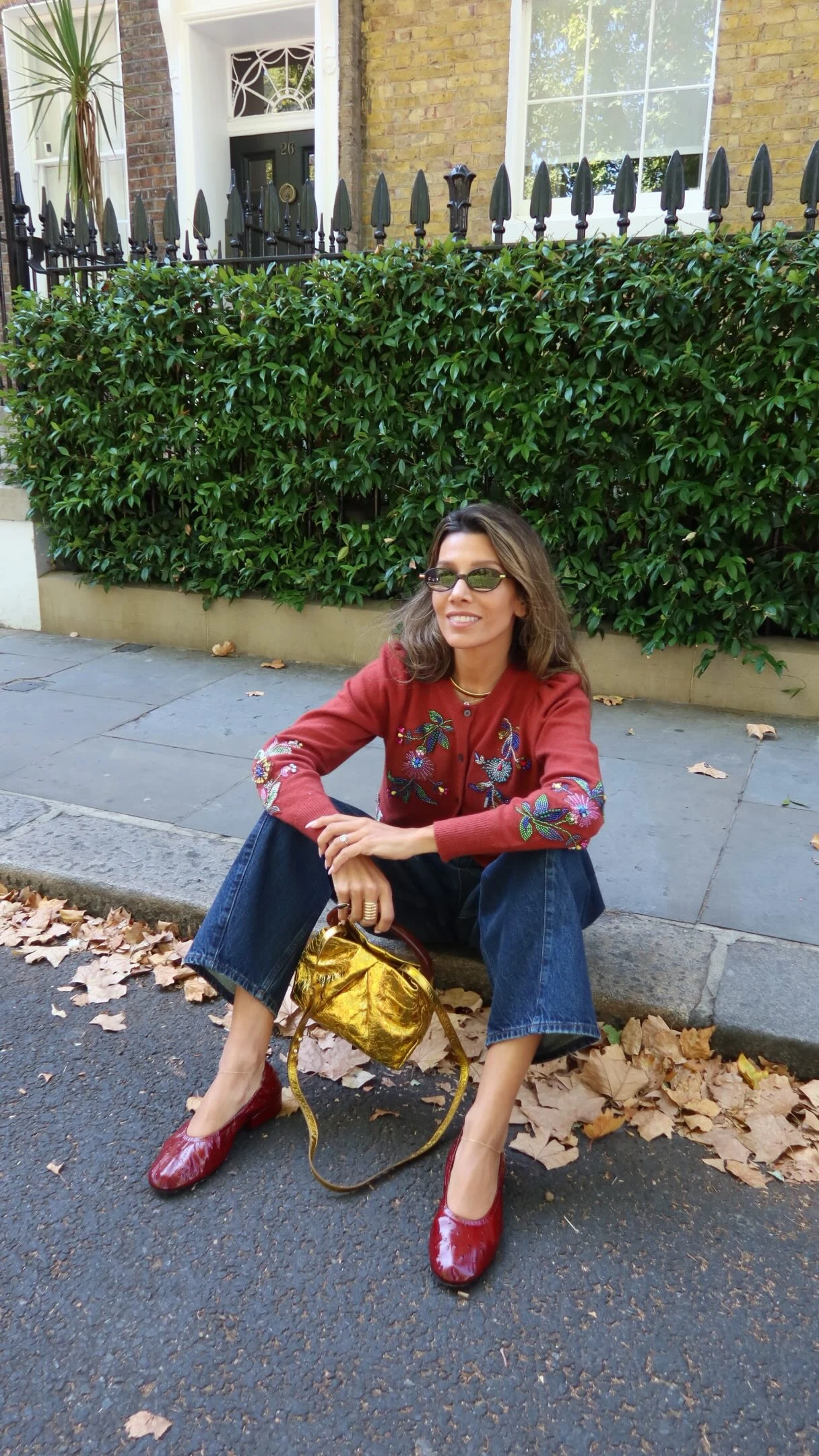 Rust-red embroidered cropped cardigan with high-waisted wide-leg blue jeans and burgundy loafers.