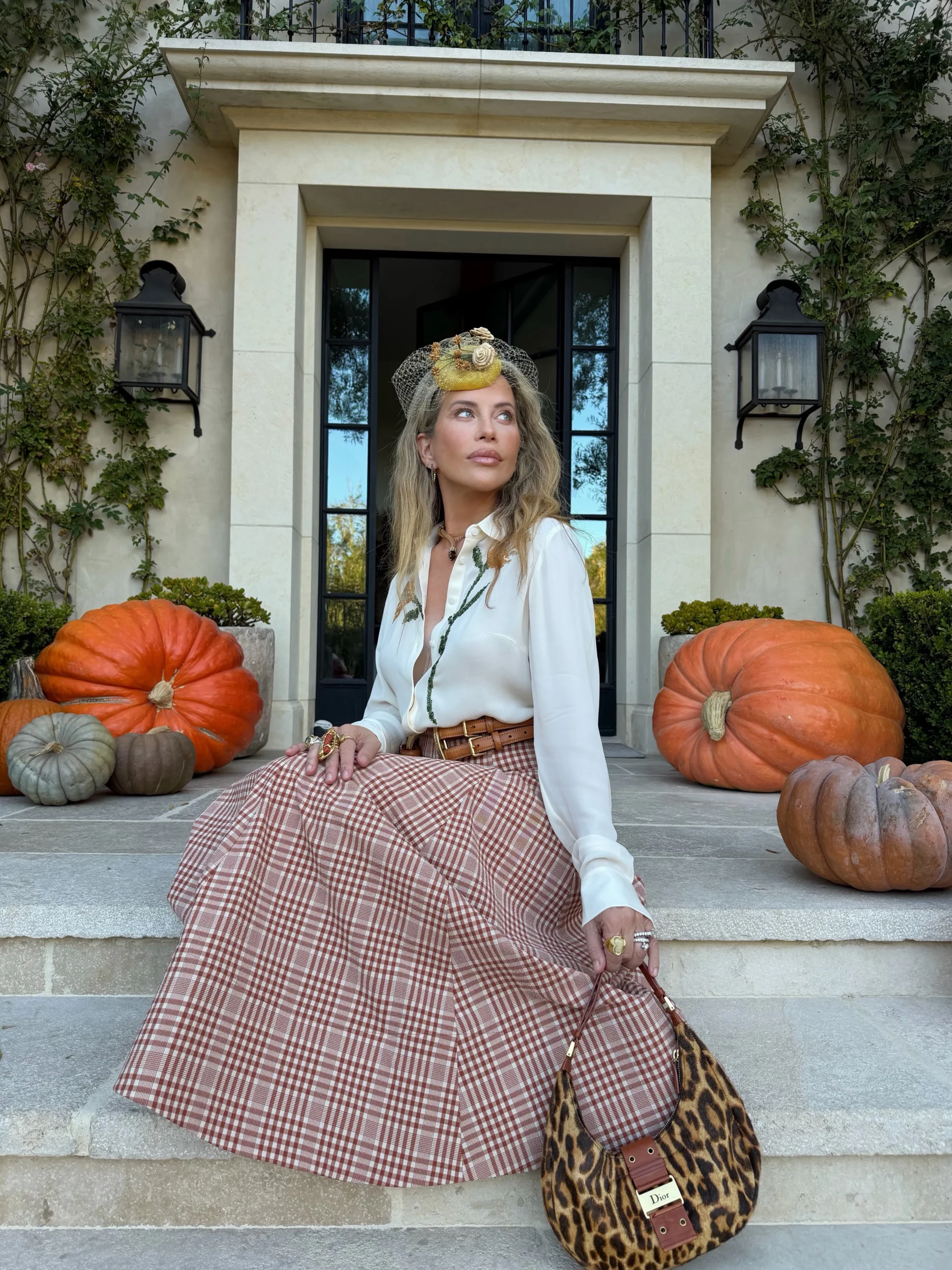 White blouse tucked into a red and cream plaid full skirt, brown belt, decorative netted hat, leopard-print bag.