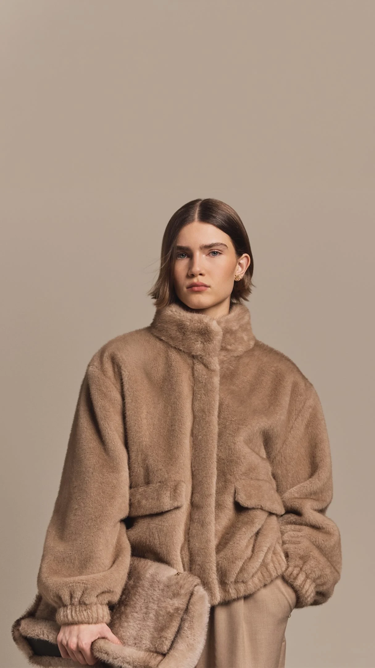 Oversized beige faux-fur bomber jacket styled with matching beige trousers and dark sunglasses.
