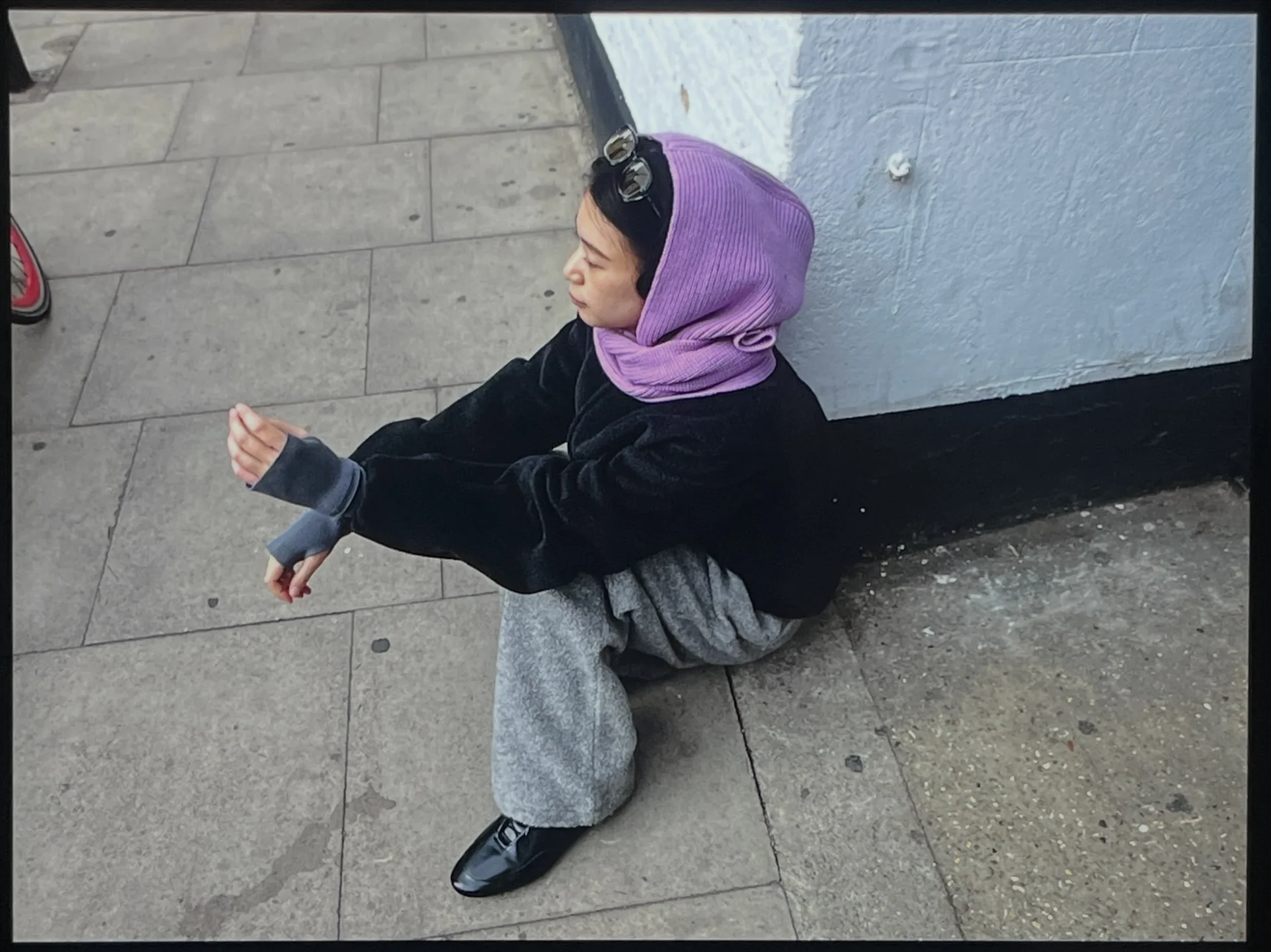 Person wearing a black fleece jacket, gray wide-leg pants, purple hooded scarf, and white sneakers.