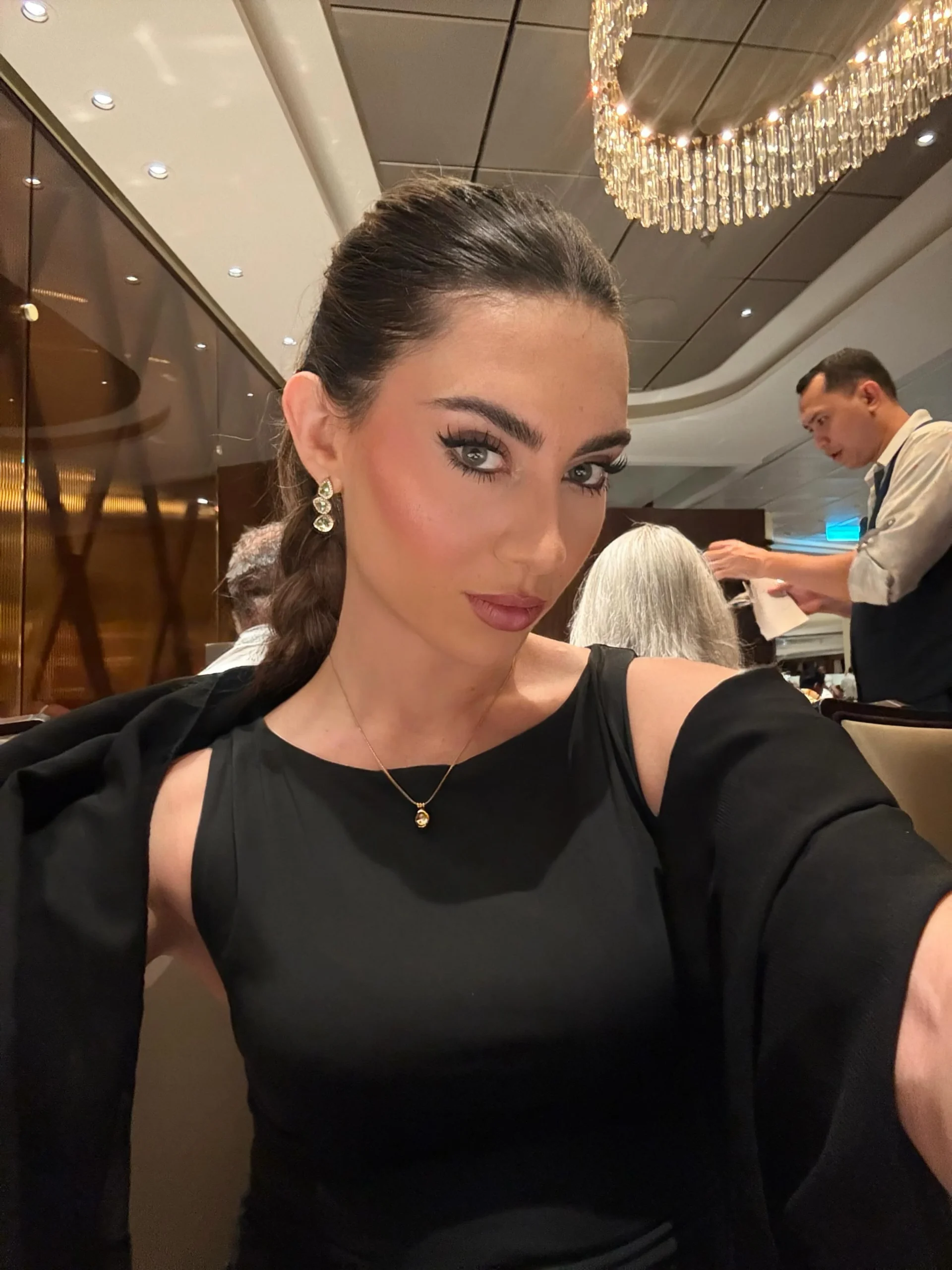 Woman wearing a black sleeveless dress with shoulder cutouts on a cruise vacation.
