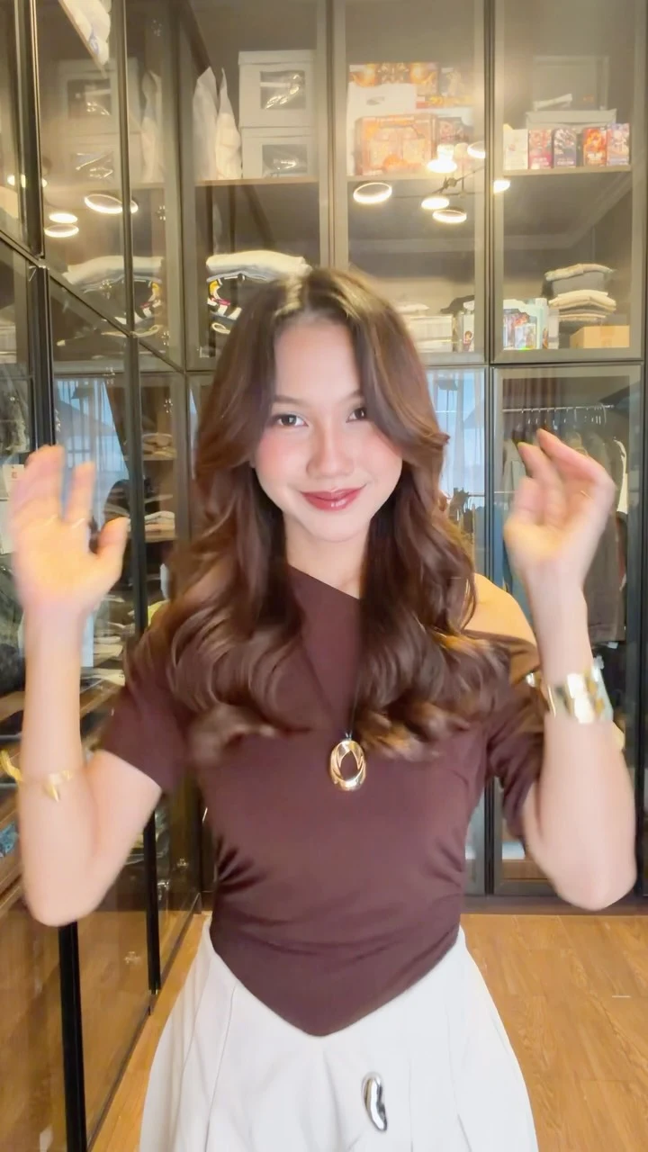 Fitted dark brown short-sleeve top with V-neck paired with a light pleated skirt and long pendant necklace.