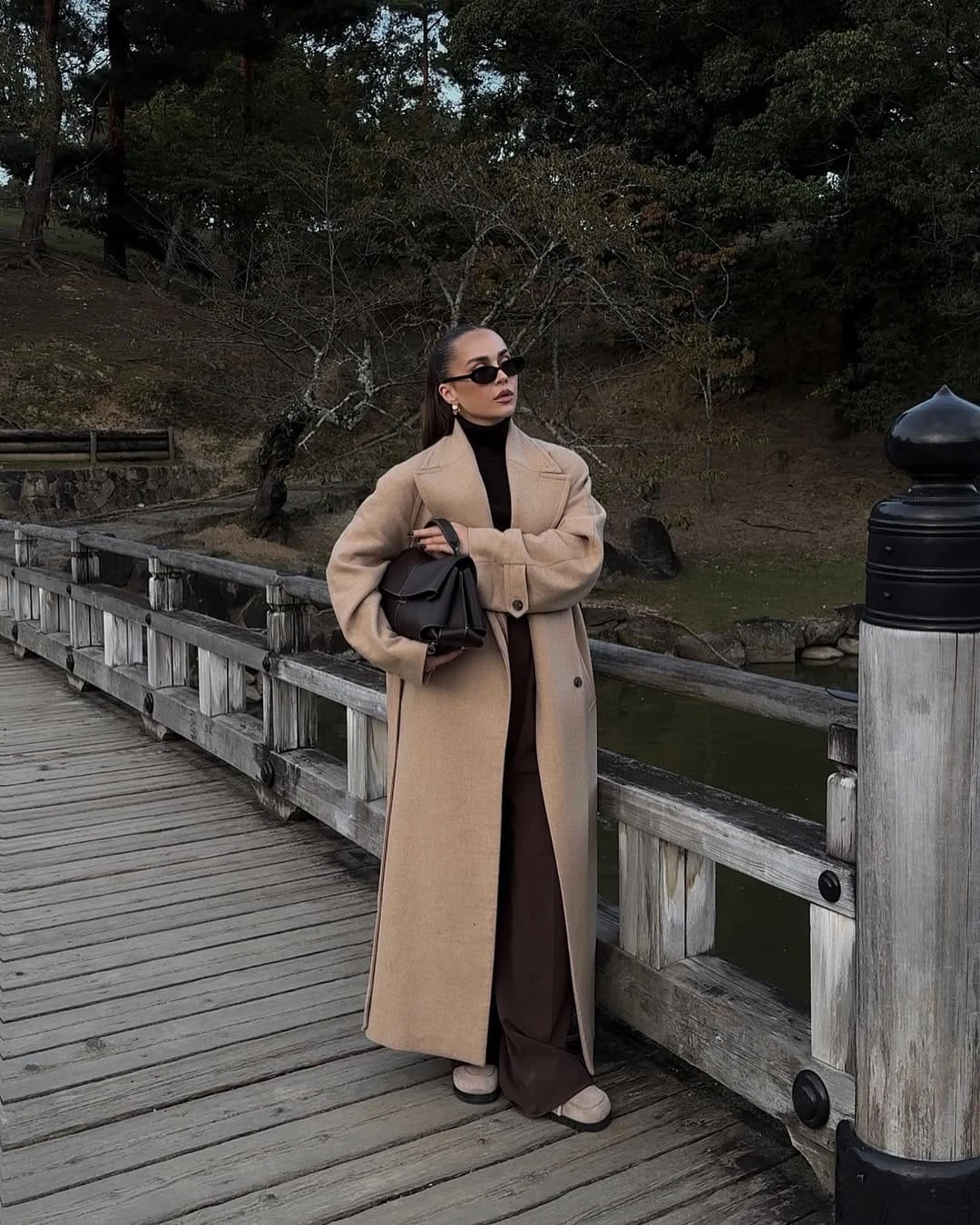 Woman wearing a camel coat over a brown turtleneck and wide-leg trousers in a minimal winter look.
