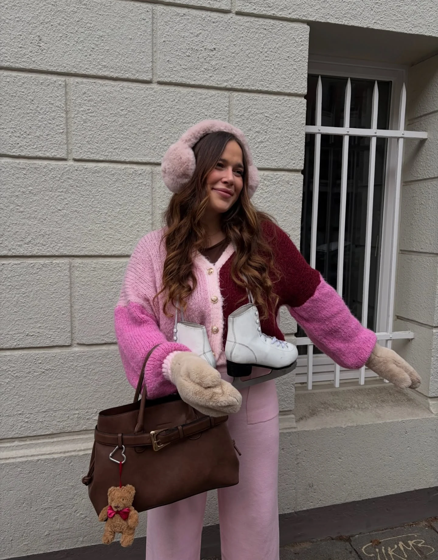 Color block chunky knit cardigan in pink and burgundy styled with light pink trousers and faux fur mittens.