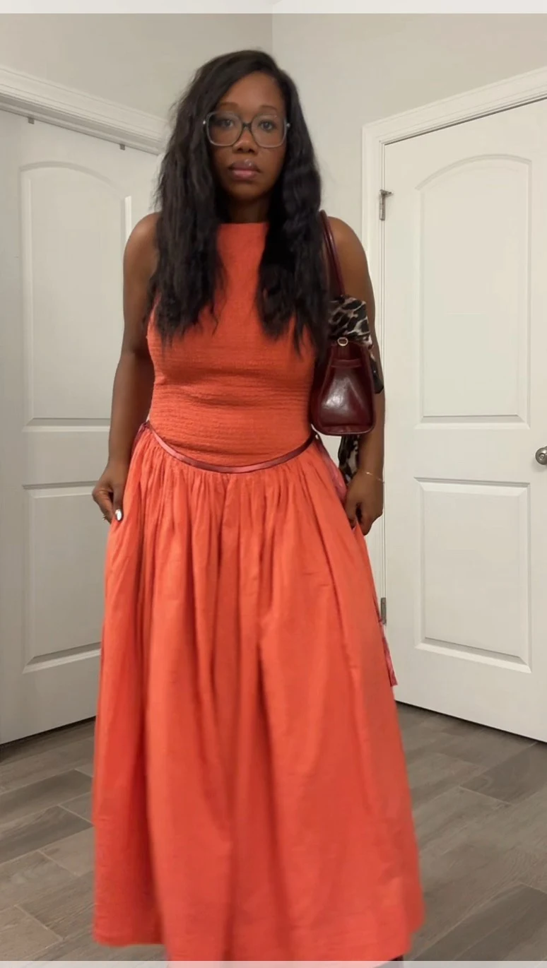 Sleeveless coral-orange top tucked into high-waisted flowing coral maxi skirt with burgundy ankle boots.