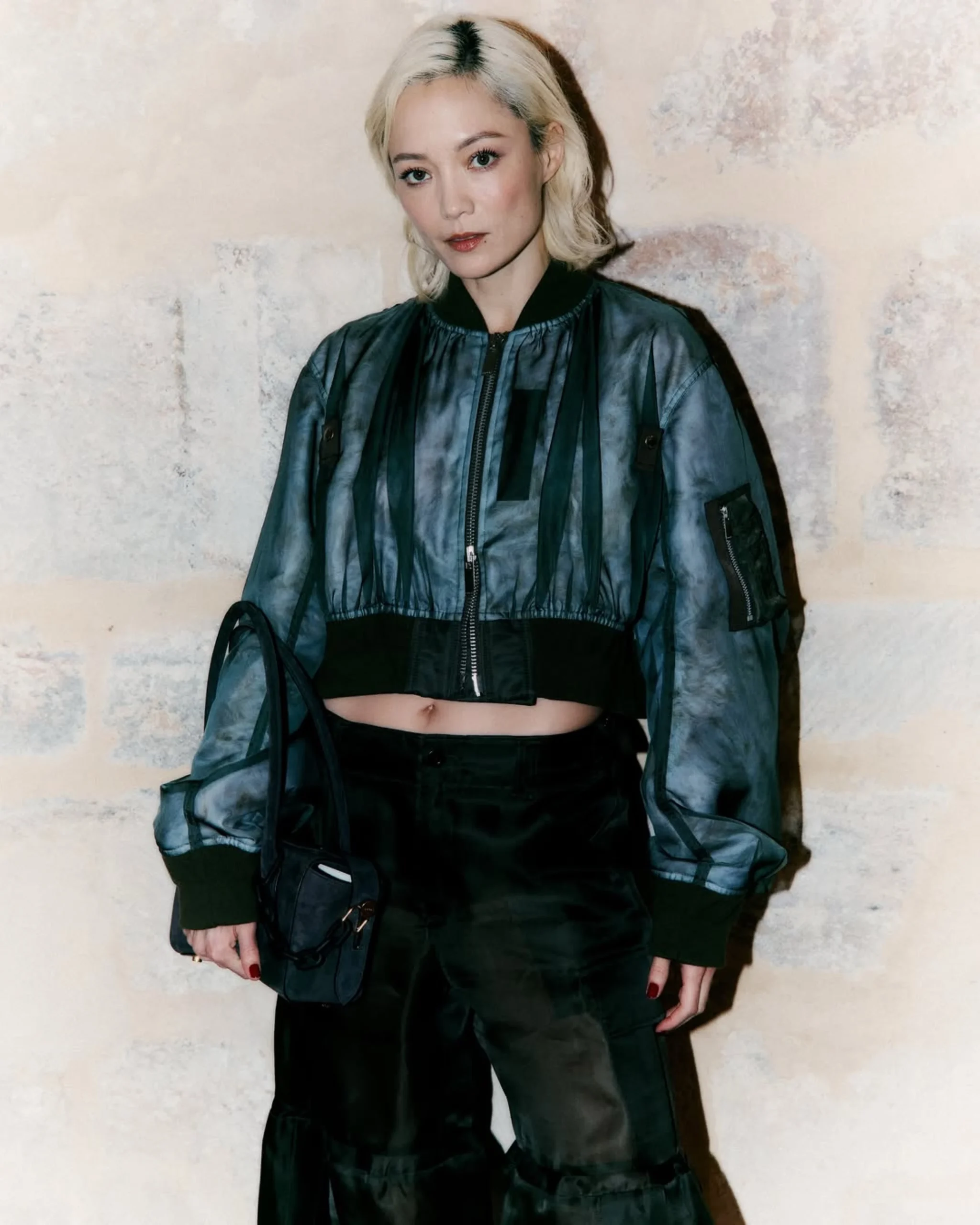 Cropped blue-gray mottled jacket with black ribbed trim over black top and loose trousers.
