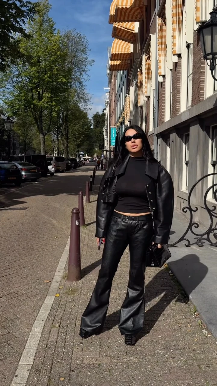 Black cropped moto-style jacket, fitted high-neck top, flared black leather pants, small black clutch, dark sunglasses