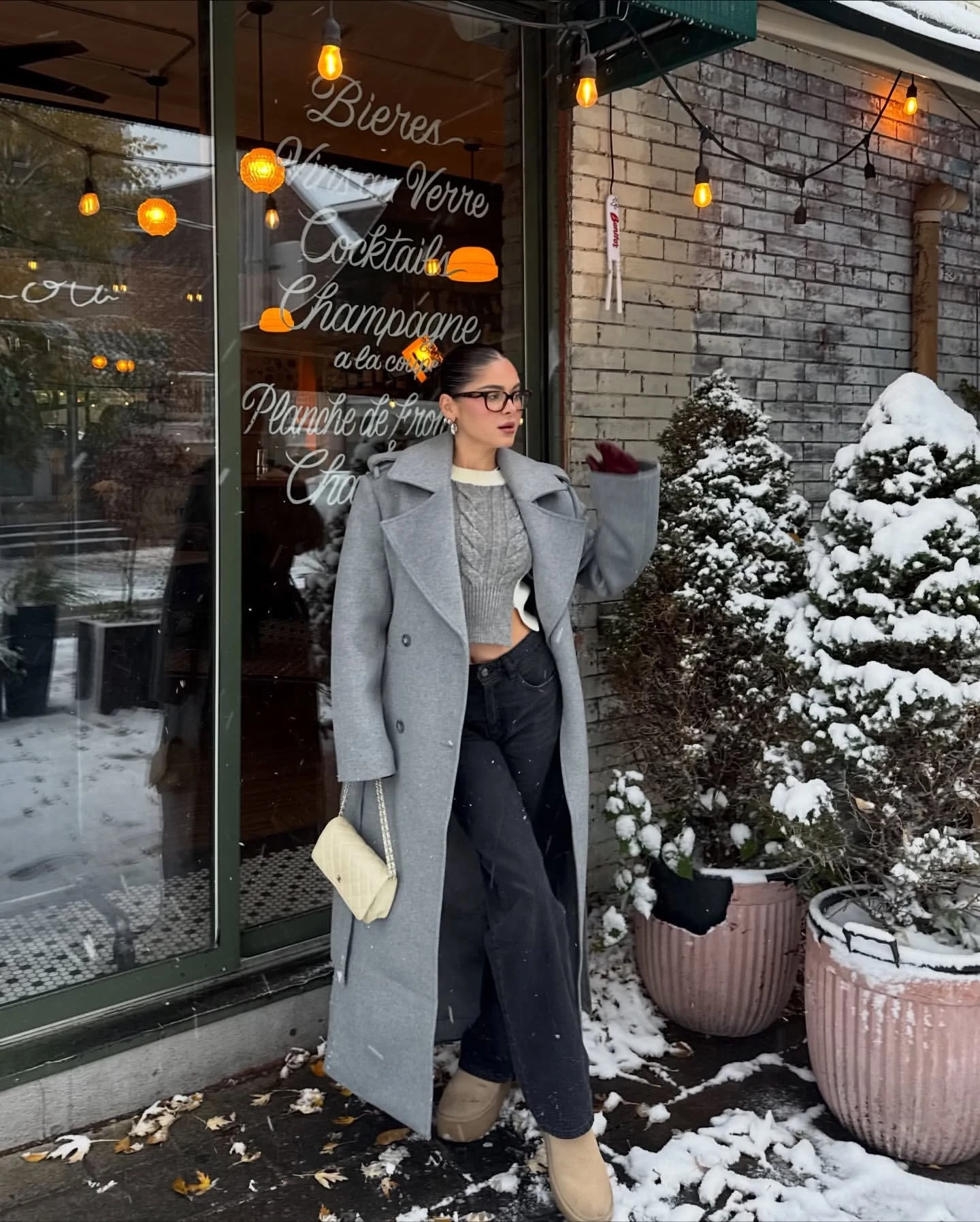 Person in long gray coat, cropped sweater, wide-leg trousers, and beige ankle boots in snow.