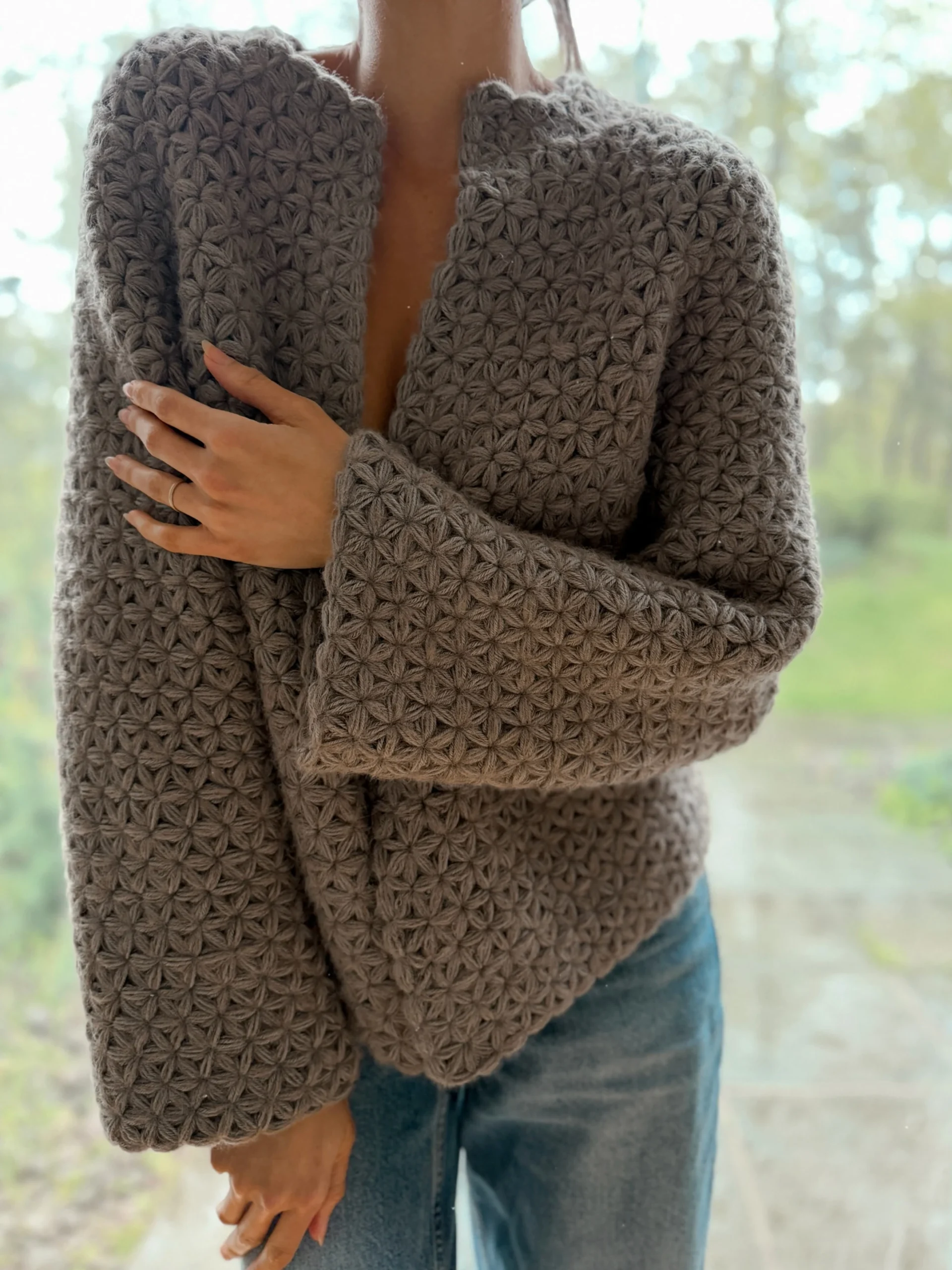 Gray textured crochet cardigan with floral stitch worn open over blue jeans.