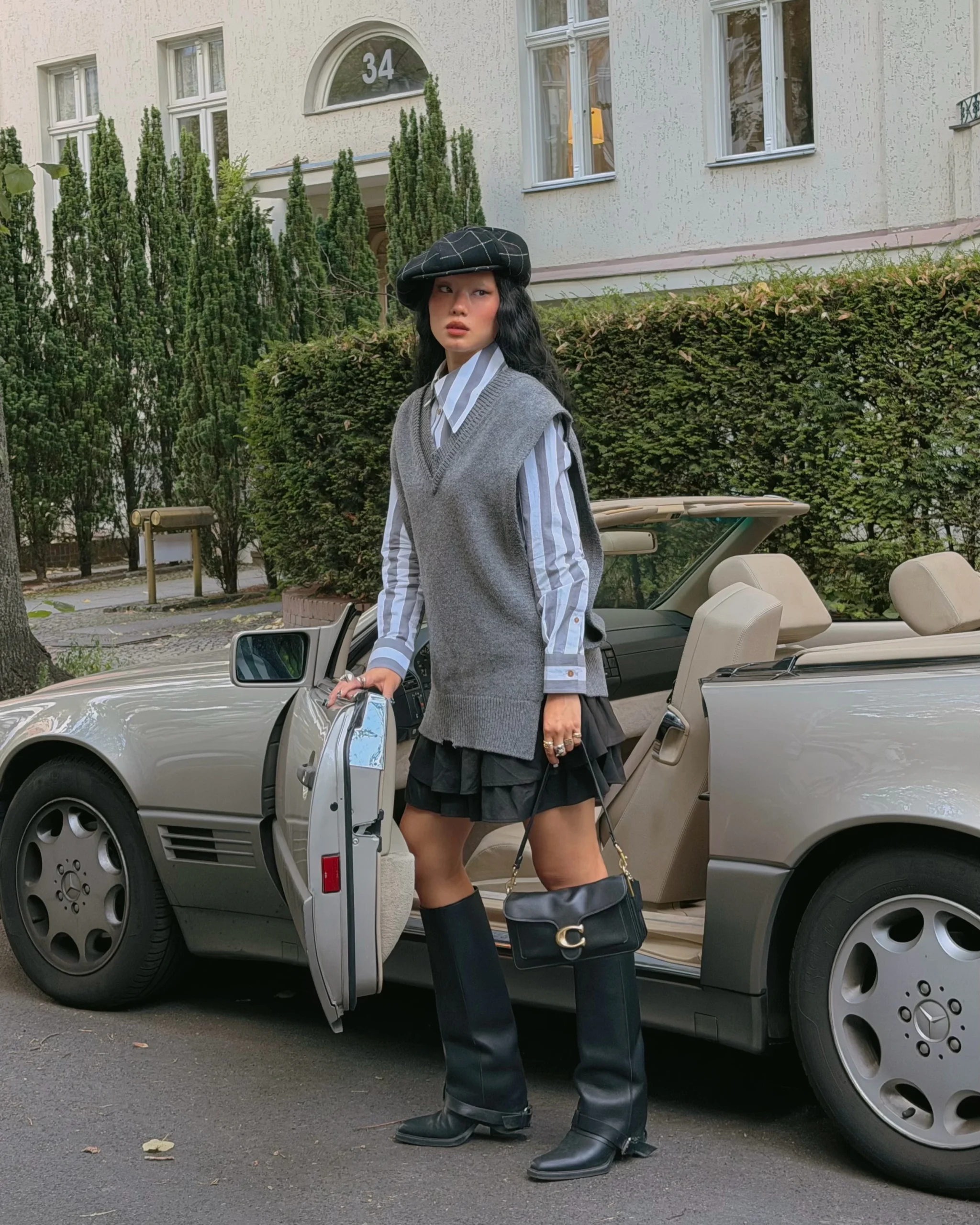Grey sweater vest over striped shirt, black ruffled mini skirt, knee-high boots, and newsboy cap.