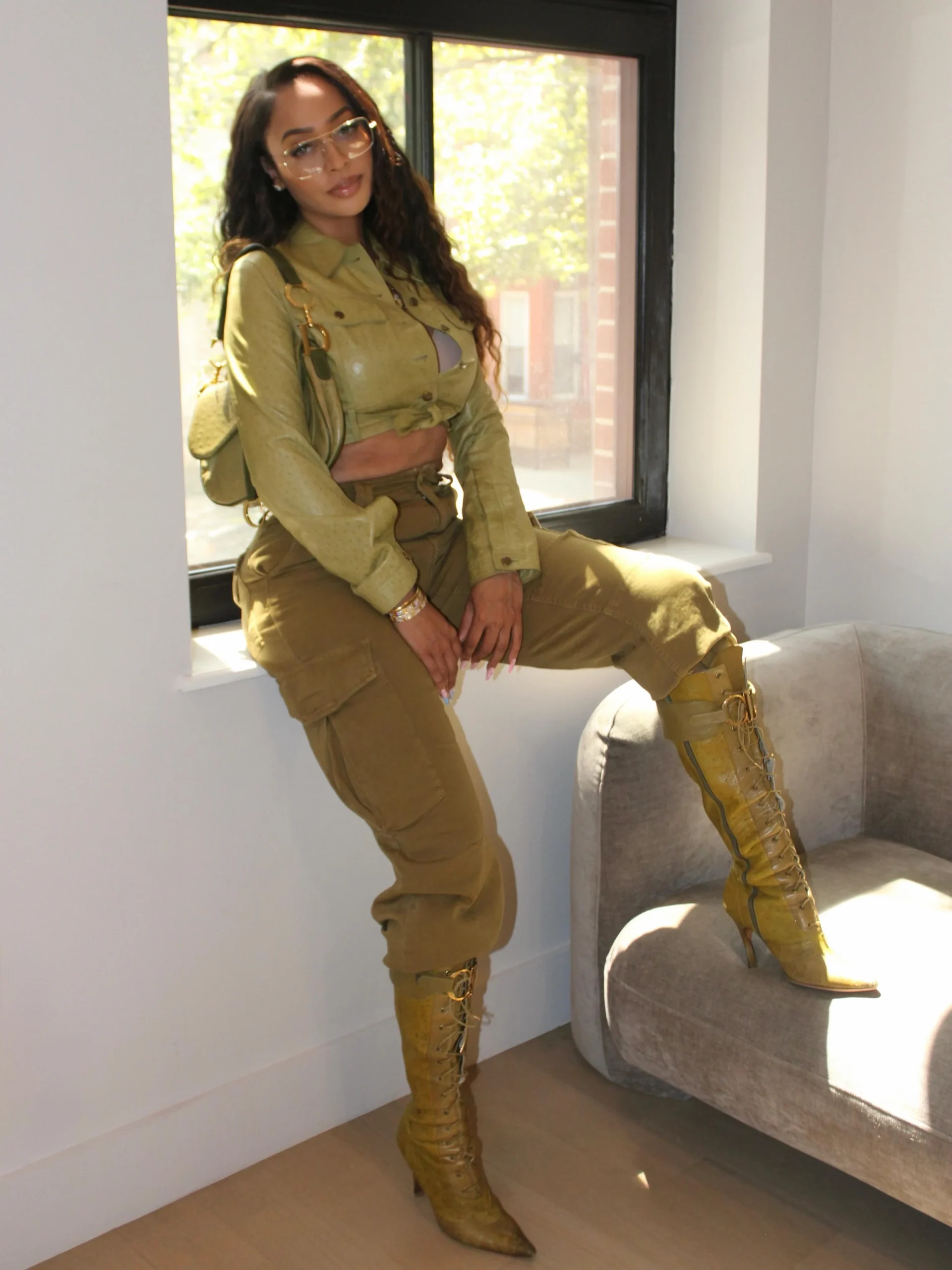Olive cropped jacket and cargo pants styled with golden lace-up boots and a small shoulder bag.