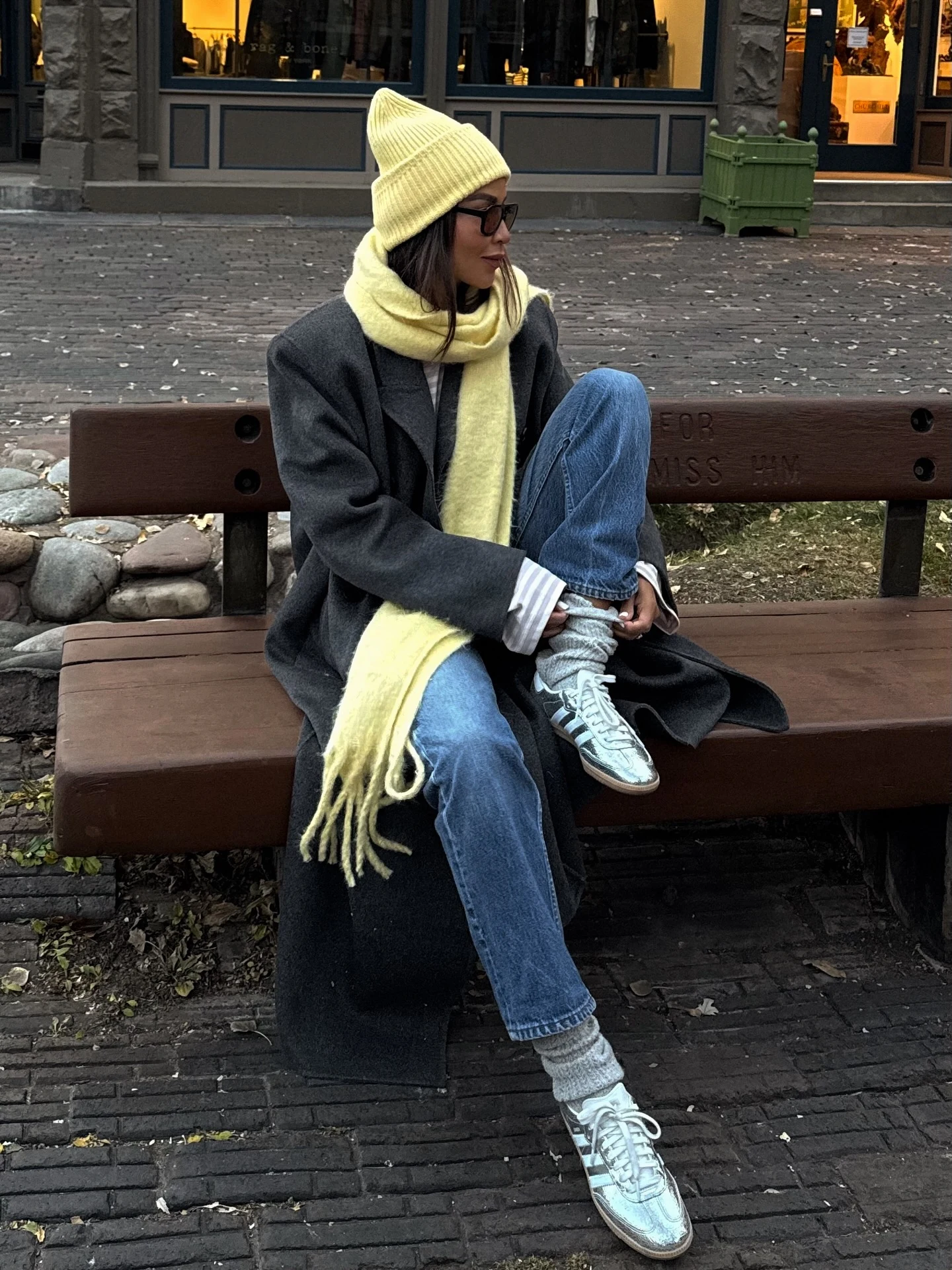 Person wearing a pale yellow beanie, fuzzy scarf, gray coat, striped shirt, and silver sneakers.