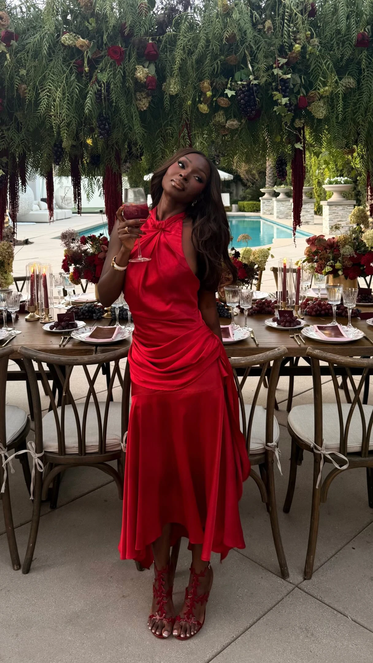 Woman wearing a vibrant red satin halter-neck maxi dress with ruched bodice and red strappy heels.