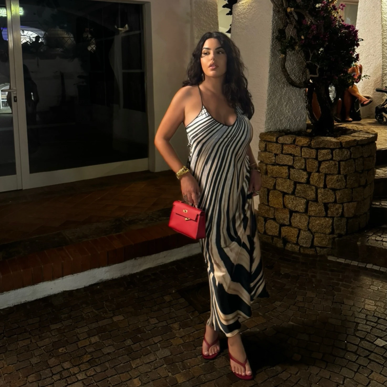 Floor-length black-and-white striped halter maxi dress styled with red sandals and a red handbag.
