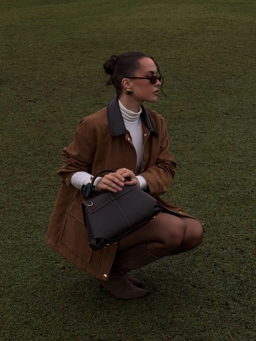 A tan suede field jacket worn over a crisp white turtleneck, with sheer tights and knee-high brown boots, is a combination that works because the suede carries an inherent softness and warmth that harder leather does not, making it feel appropriate for the countryside in a way that a city-style leather jacket might not. The white turtleneck underneath the suede adds a crispness and contrast at the collar that keeps the look clean and considered, and the sheer tights introduce a femininity that stops the field jacket from reading as purely utilitarian. I love this as a heritage-inspired look that manages to feel genuinely modern and elegant rather than costume-adjacent.
