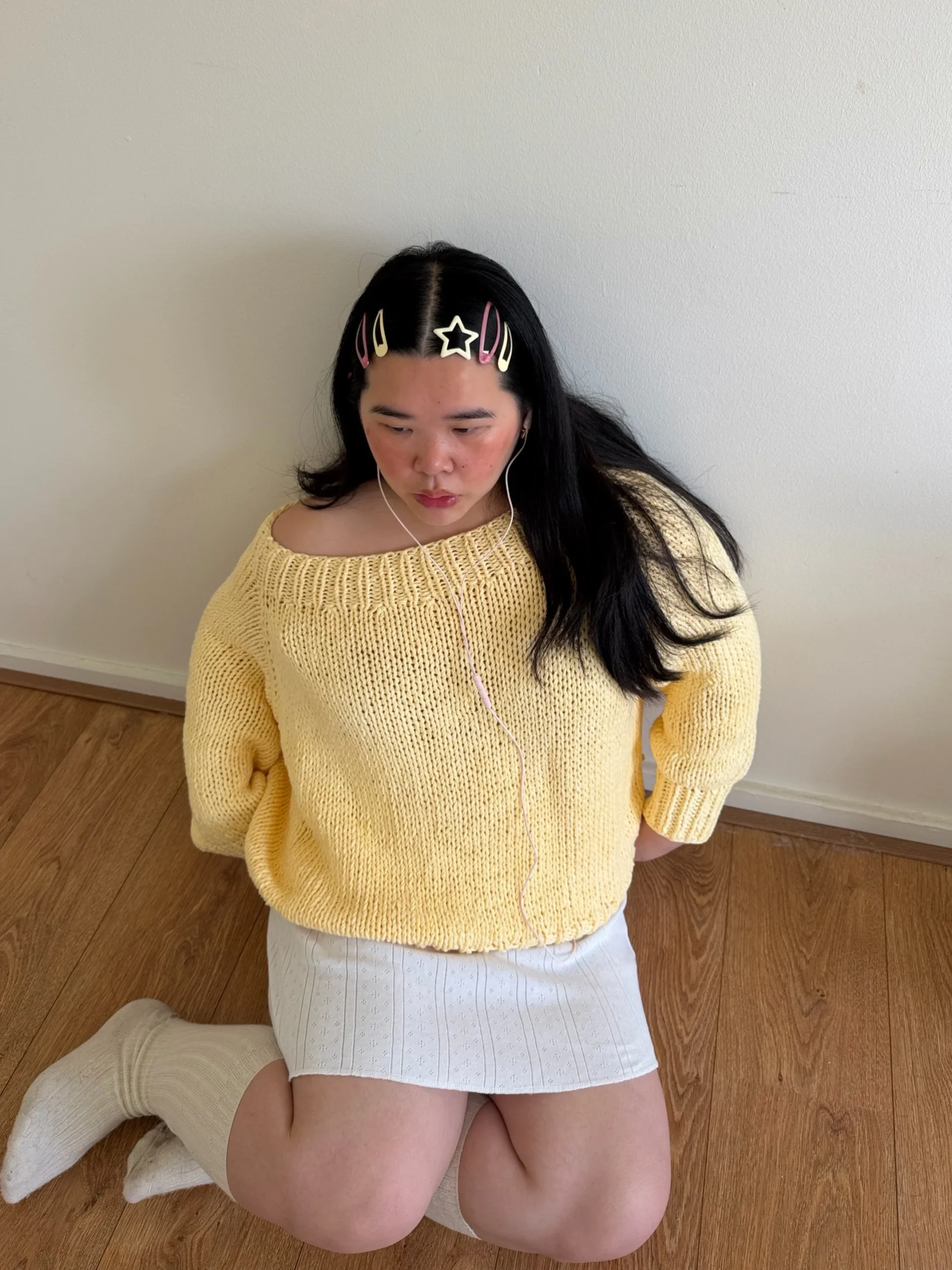 Pale yellow off-shoulder chunky knit sweater styled with a short white perforated skirt and white ribbed knee-high socks.