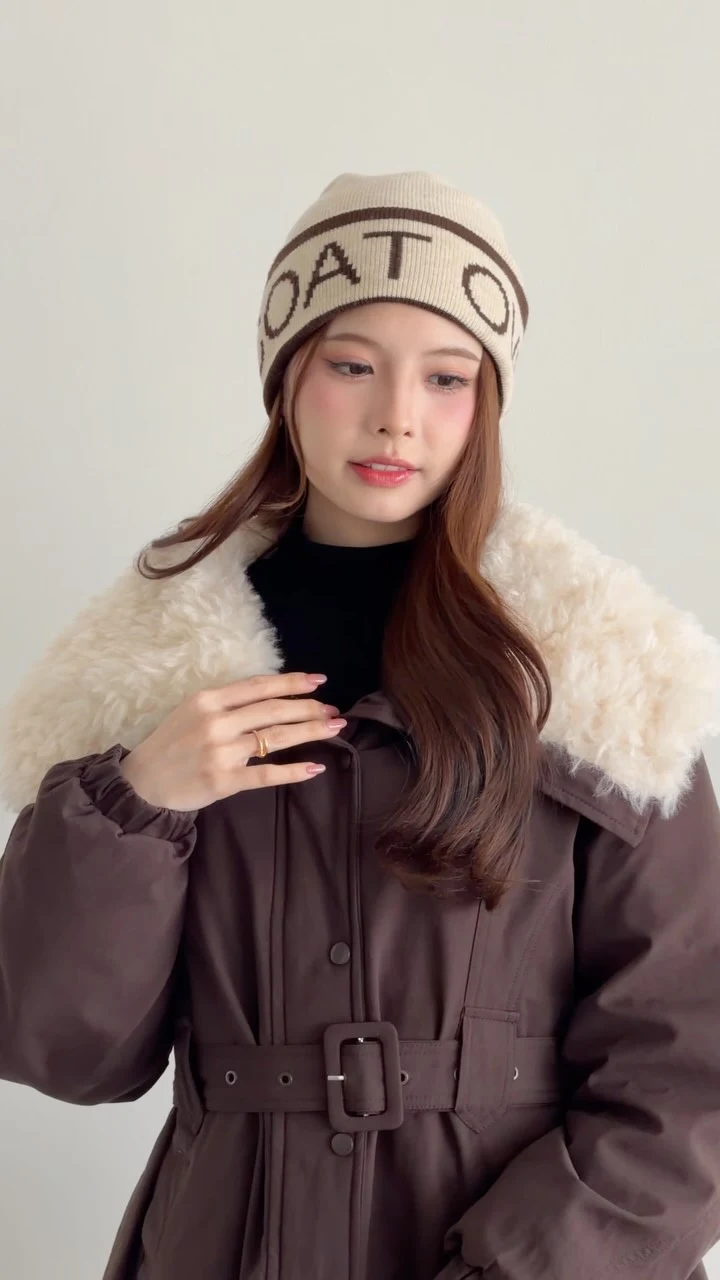 Person in a belted brown puffer coat, cream collar, black turtleneck, mini skirt, and knee-high boots.