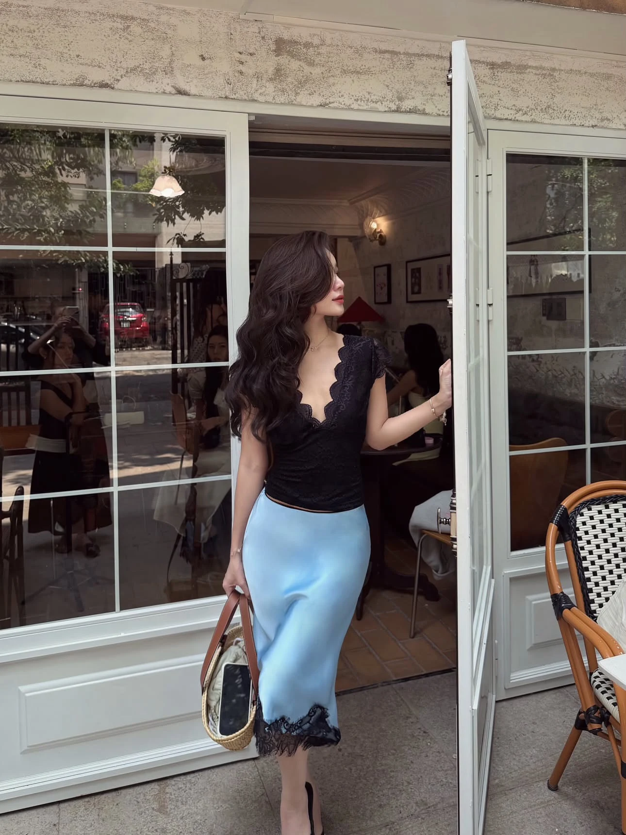 Fitted black lace top with scalloped neckline paired with a pale blue midi skirt and woven bag.