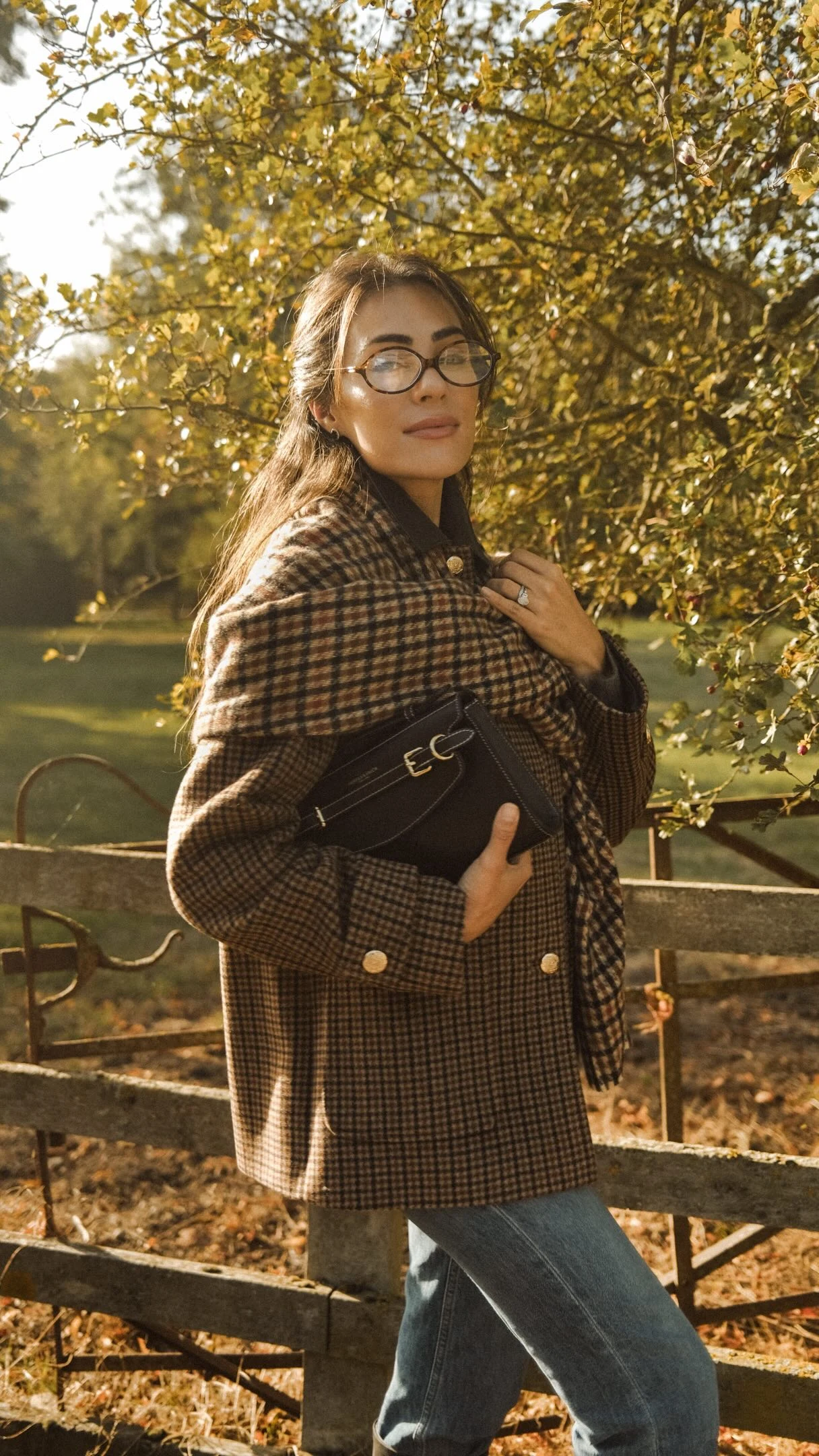 Oversized brown checked blazer with shoulder drape, blue jeans, and black gold-clasp bag.