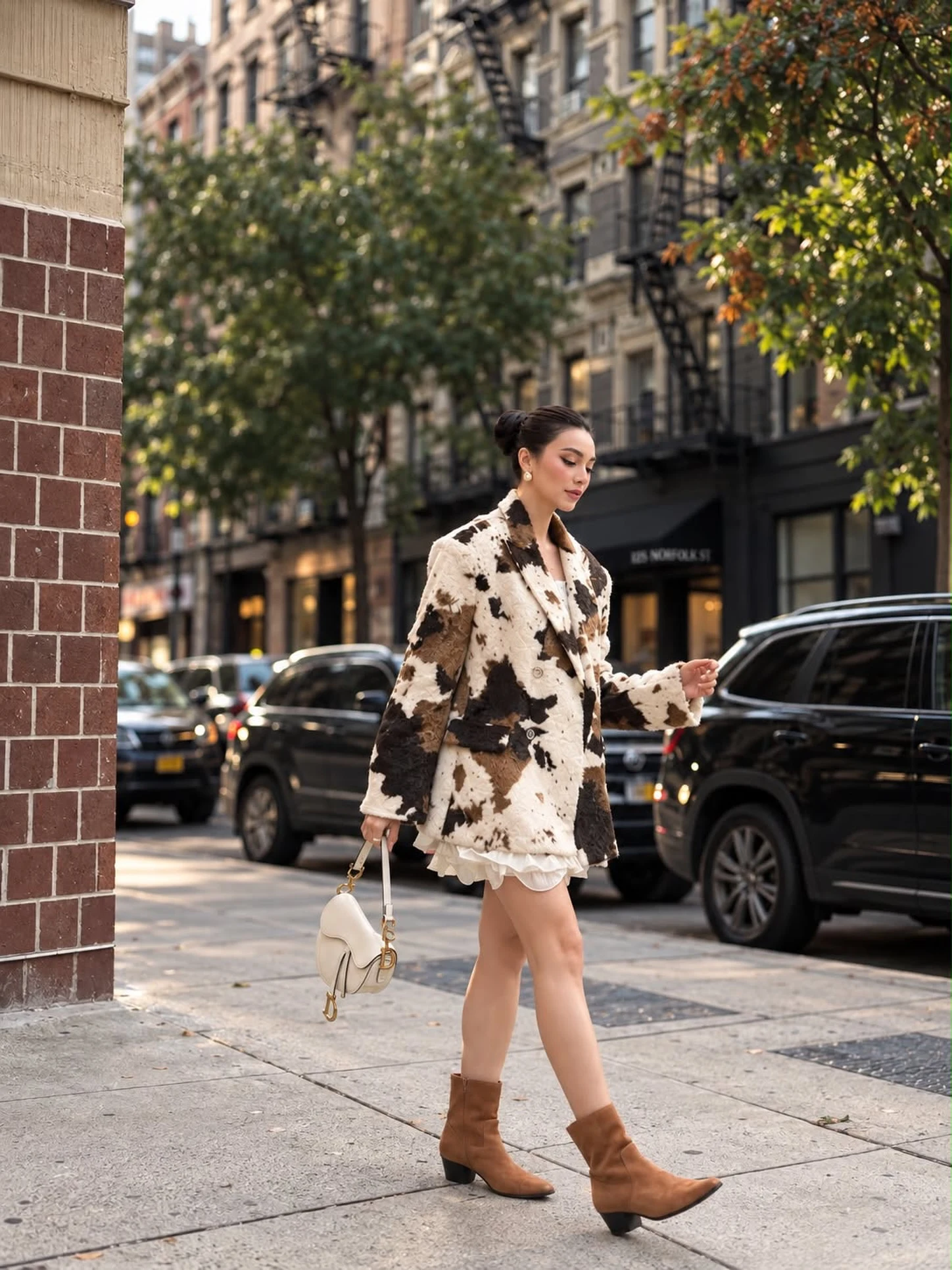 Cow print knee-length coat over a white ruffled dress with tan suede ankle boots.
