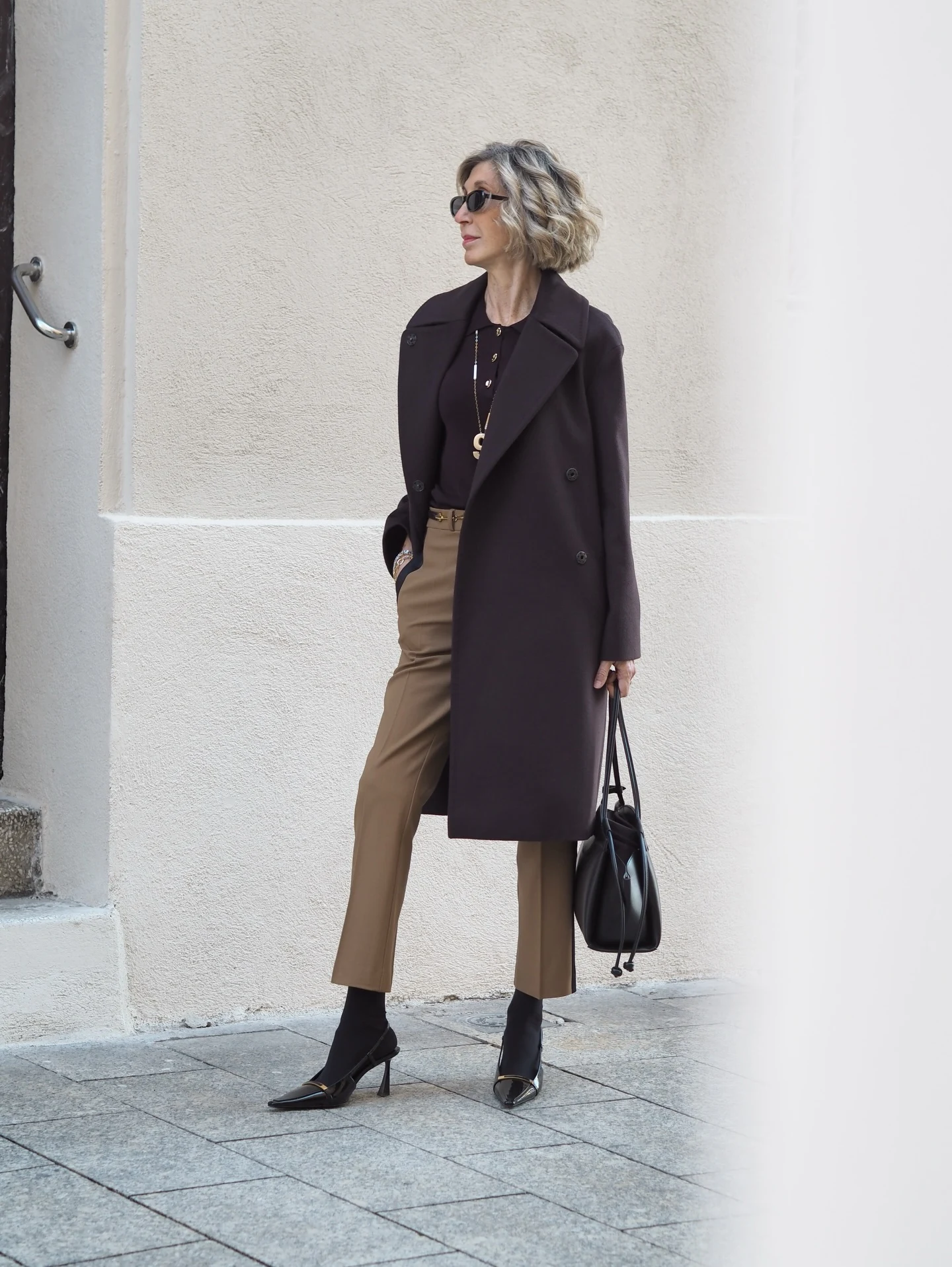 Dark brown wool coat worn open over a black polo, camel striped trousers, and black slingback heels.