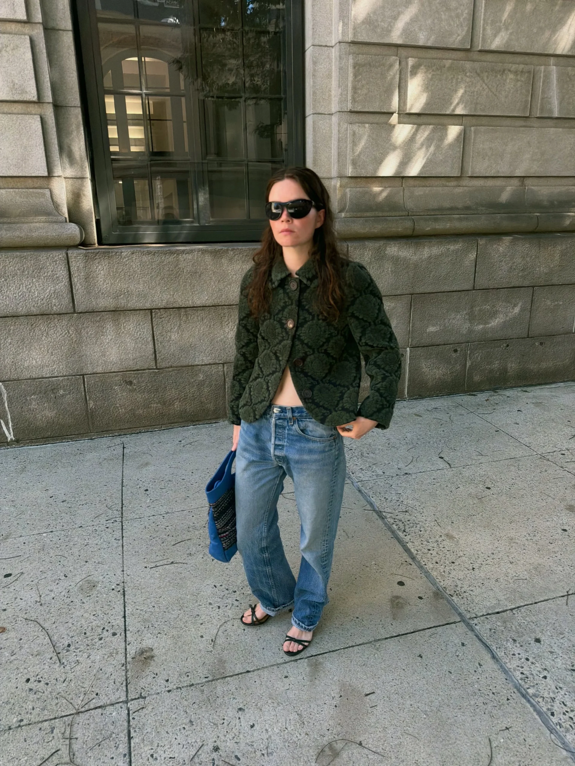 Dark green floral cropped jacket buttoned over light blue wide-leg jeans with black strappy sandals.