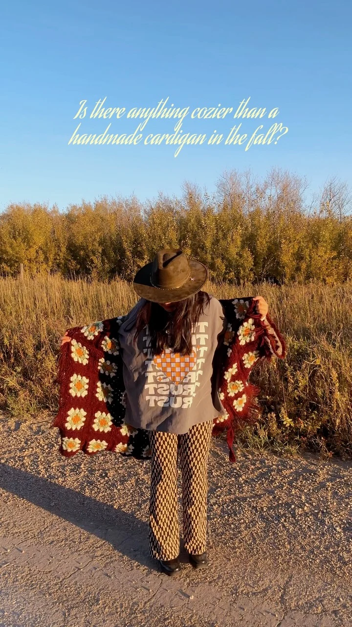 Dark red floral crochet cardigan over gray tee and geometric wide-leg trousers with brown hat.