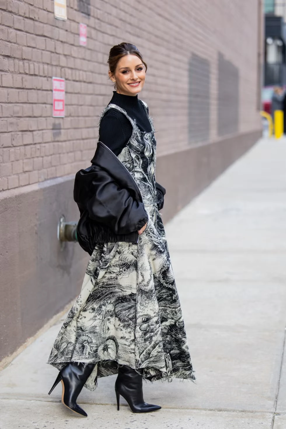 Olivia Palermo wears a graphic print dress, bomber jacket, black turtleneck, and boots in NYC.