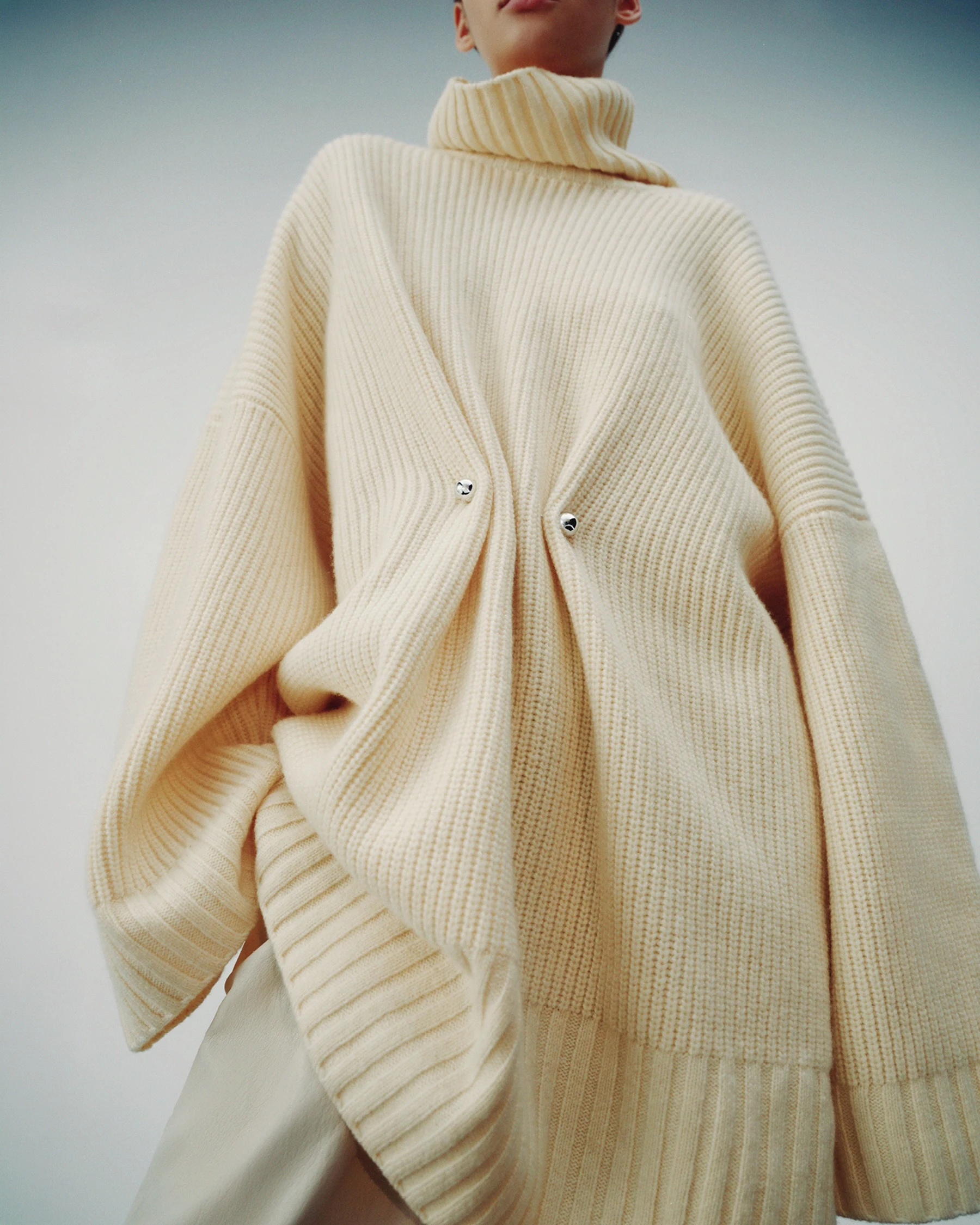 Person layering an ivory ribbed turtleneck under a matching oversized V-neck cardigan with dropped shoulders.